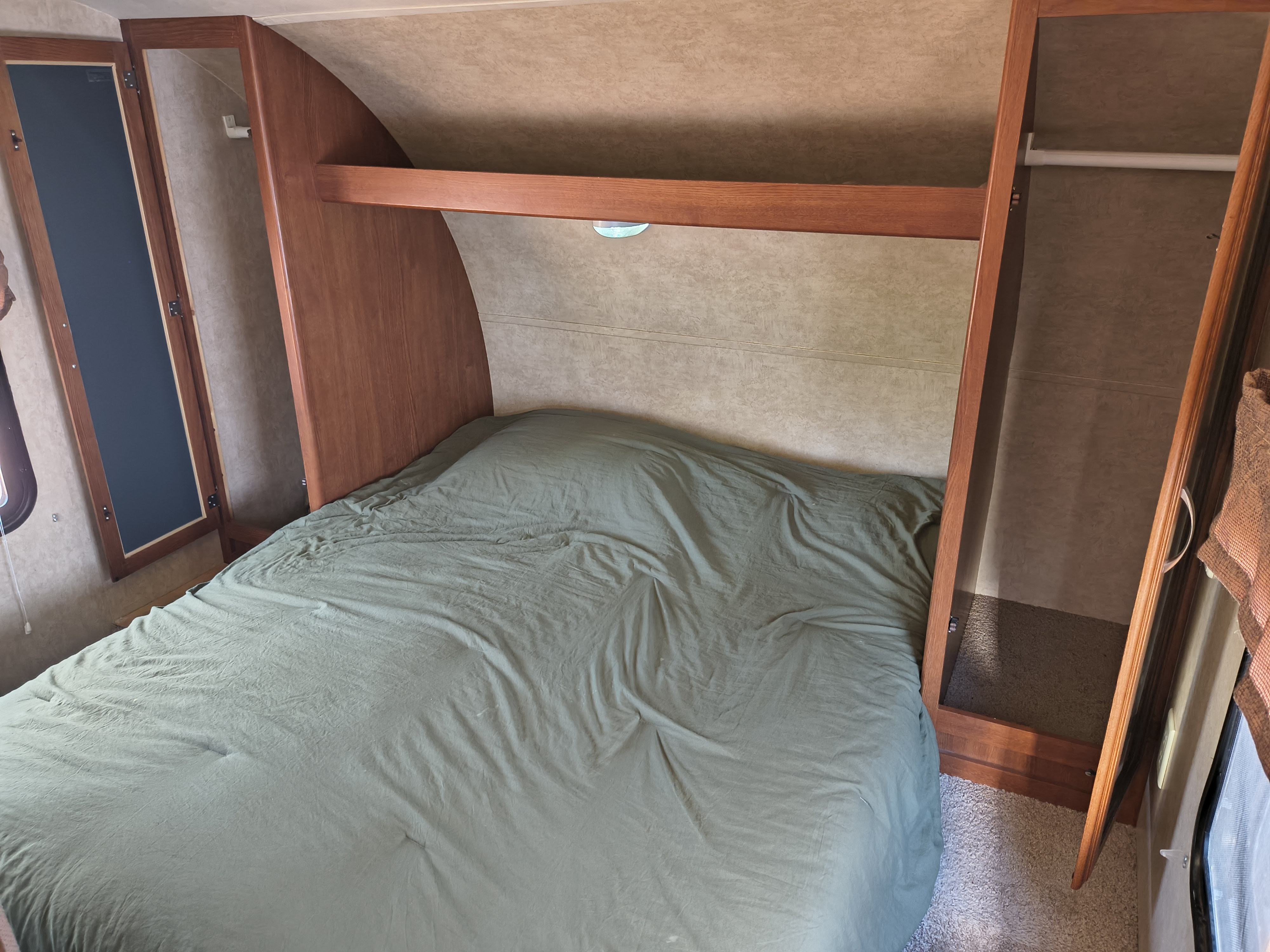 Compact **rv rental** bedroom with a bed, green bedding, overhead shelf, and open closets for storage.. Forest River Wildwood X-Lite 2015