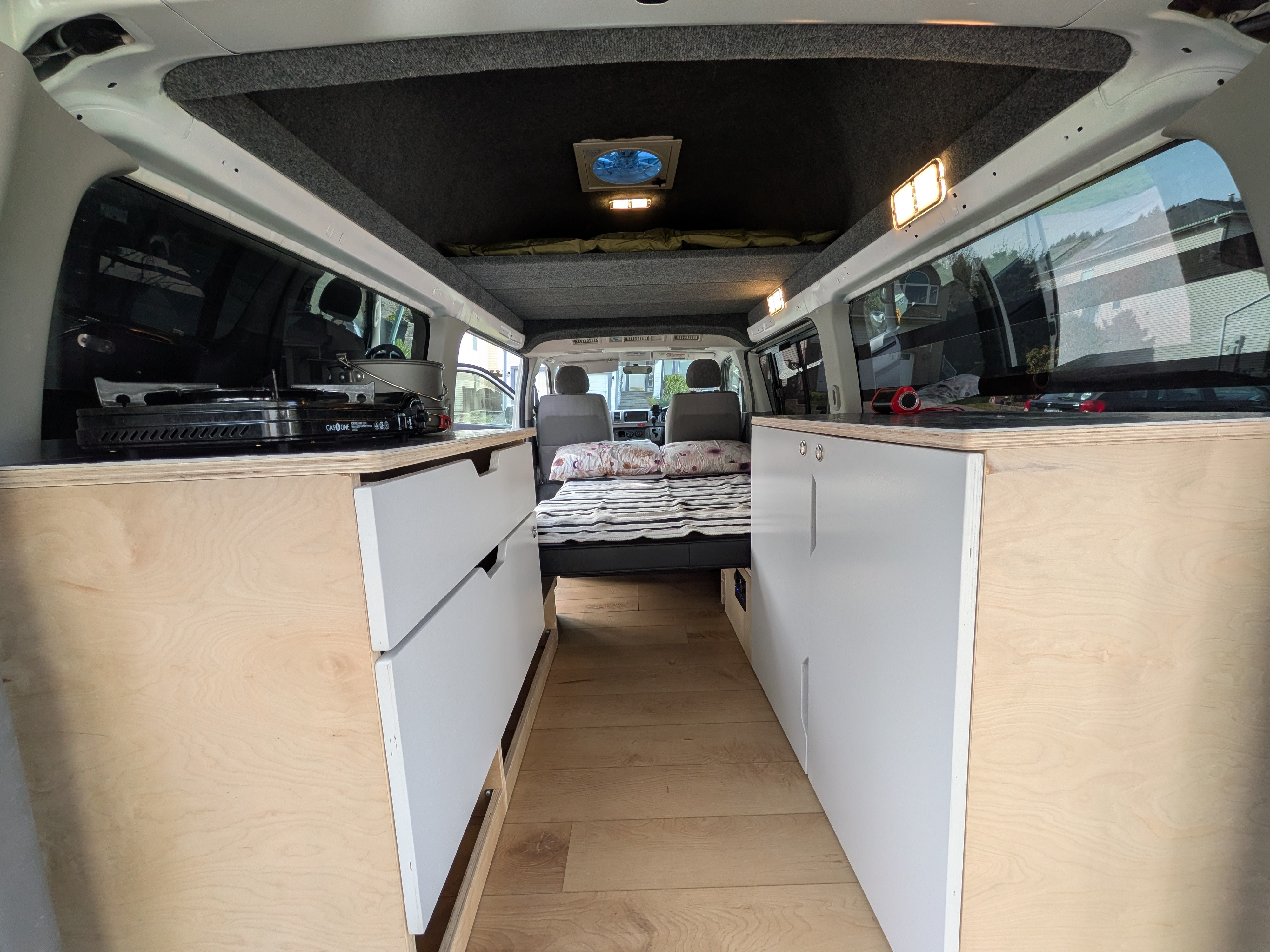 Cozy RV rental interior with bed, built-in cabinets, kitchenette with stove, and wooden floor. Perfect for adventure.. Toyota Hiace 2005