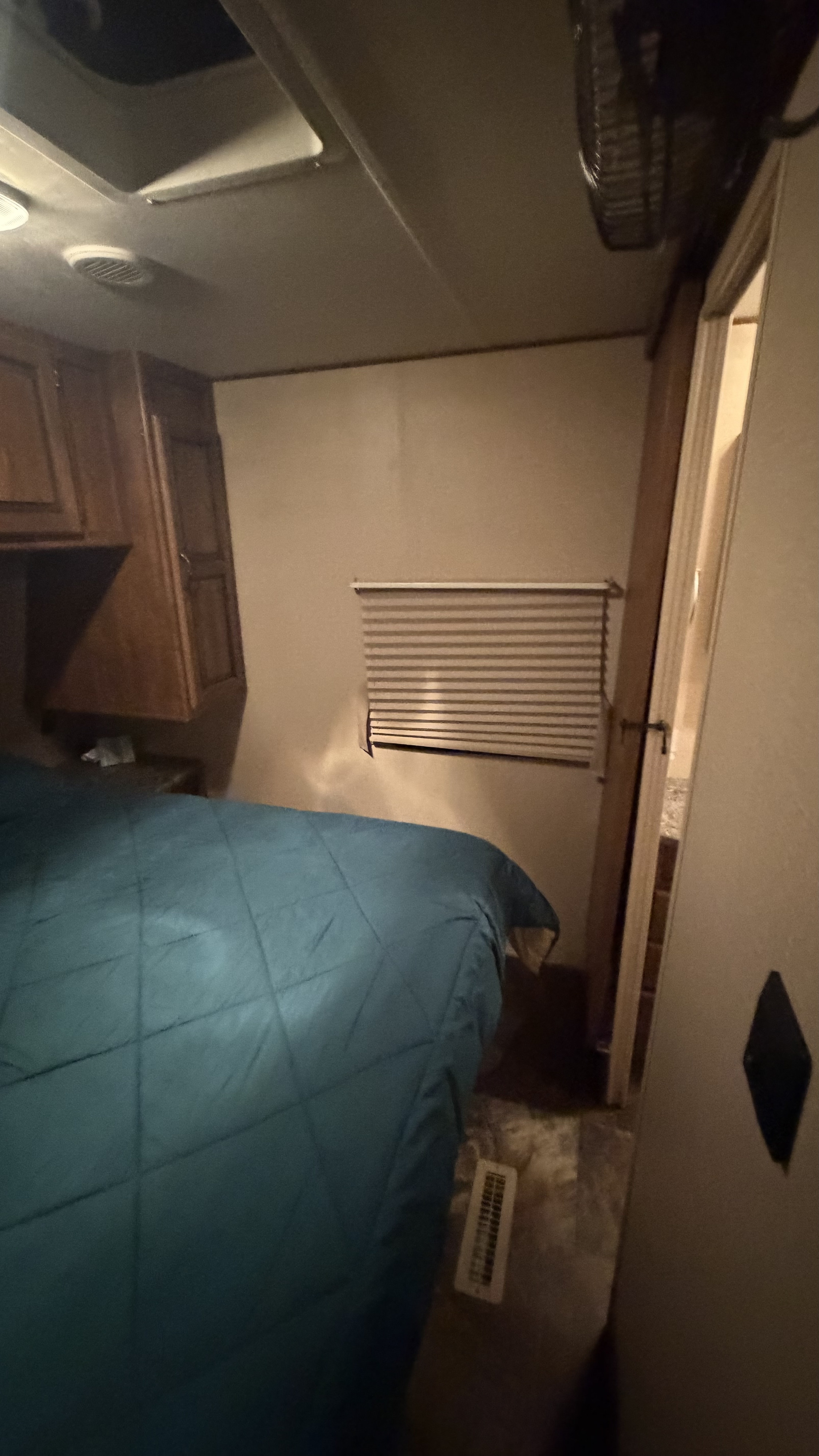 Inside an RV rental: a cozy bedroom features a blue quilted bed, wood cabinets, window blinds, & a ceiling fan.. Crossroads RV Rezerve 2015