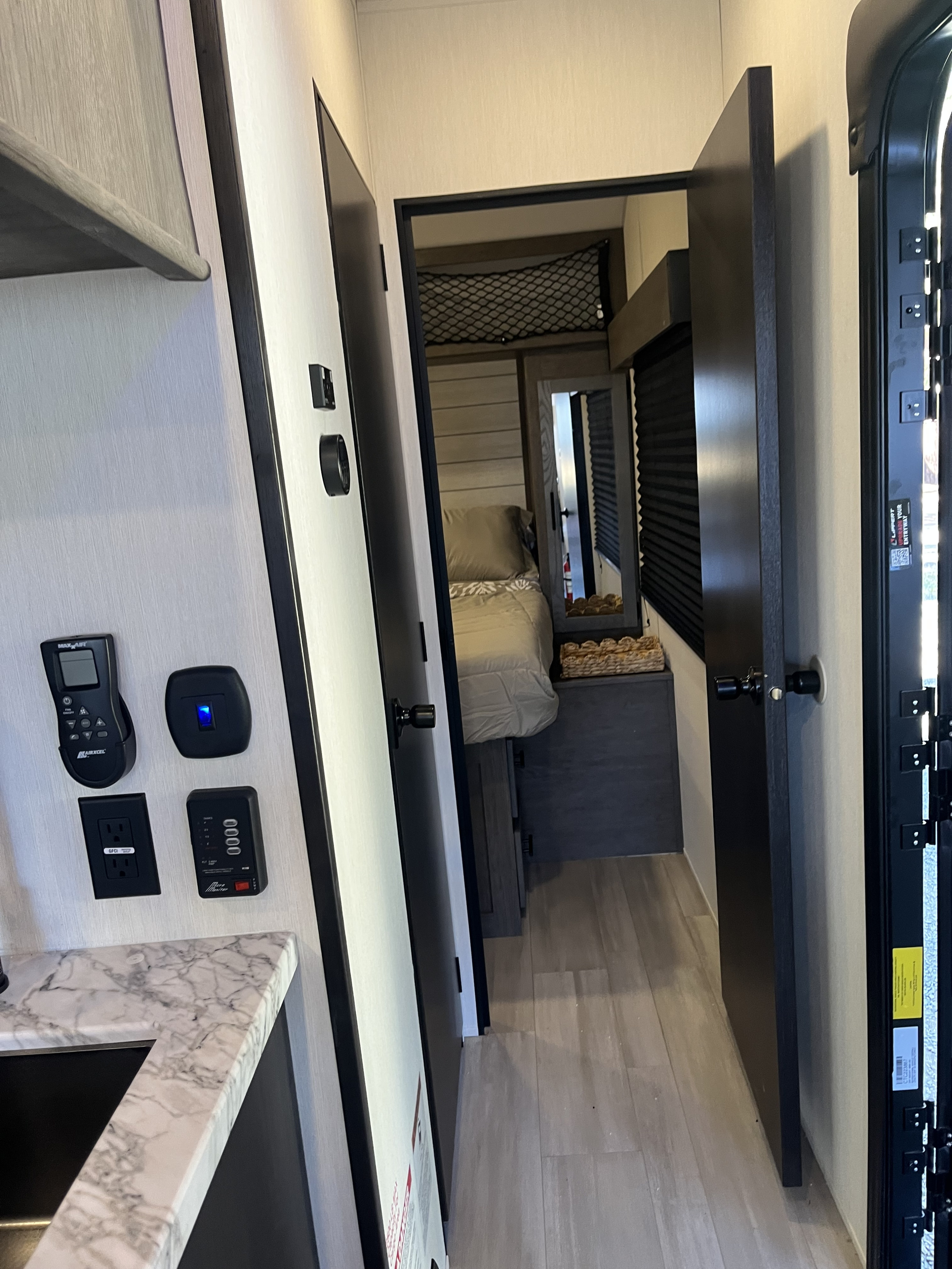 RV rental interior: hallway to a compact bedroom, with controls, sink, and storage net. A functional camper living space.. Forest River Wolf Pack 2026
