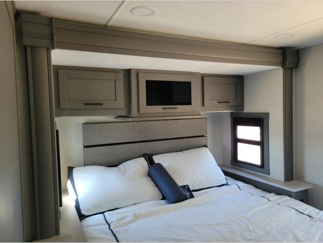 This modern RV rental bedroom features a cozy bed, overhead cabinets, a TV, and a window.. Forest River Coachmen Pursuit 2025