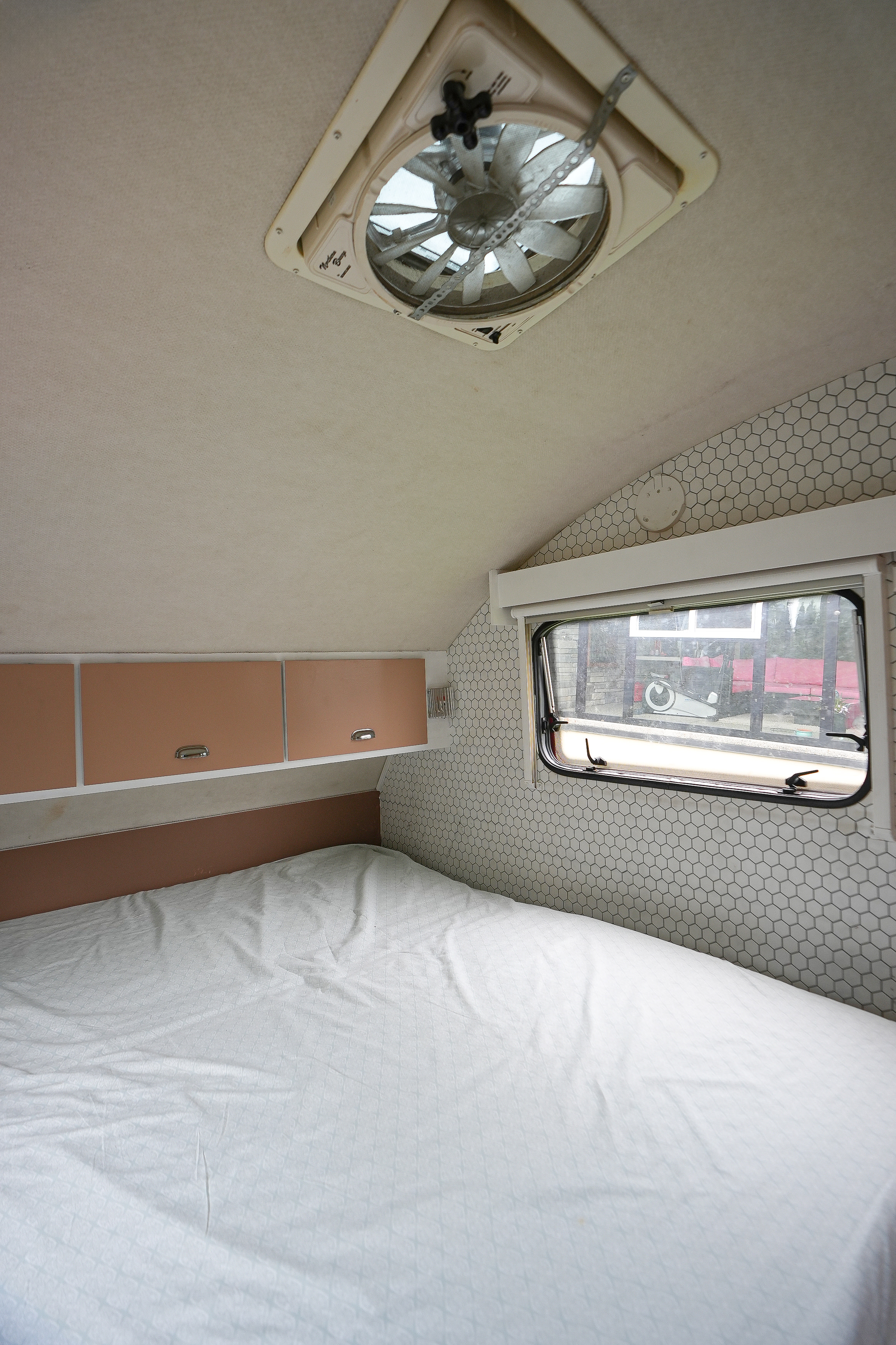 Inside an RV rental: a comfortable bed, peach cabinets, hexagon wall, window view, and ceiling vent.. Stirling T@B 320 Teardrop Micro Traile 2014