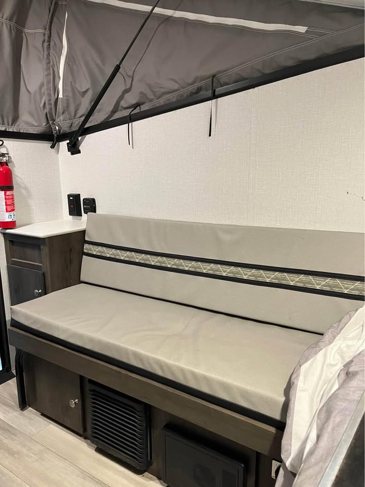 This RV rental's interior offers a cozy bench seat, a folding bed section above, and a fire extinguisher for safety.. Forest River V-Tec Lifted Camper & Toy Hauler 2023