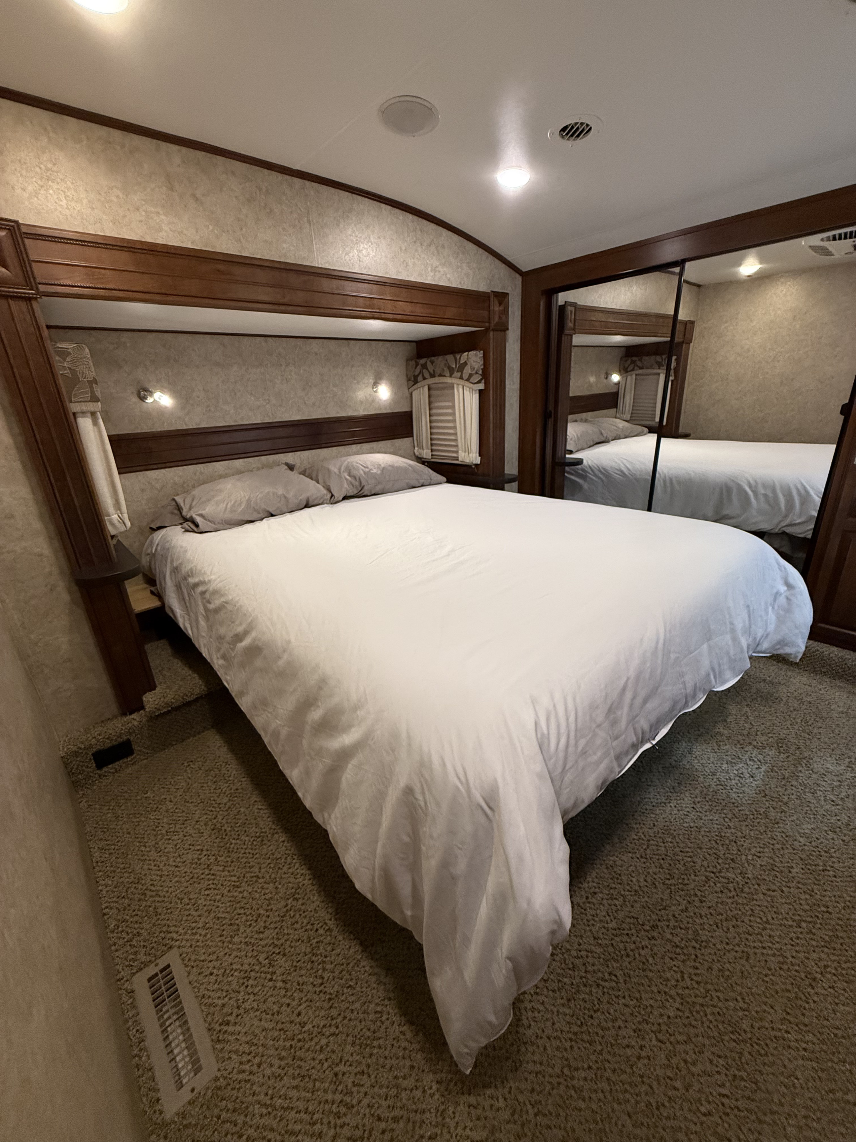 Cozy bedroom in an rv rental, featuring a large bed, wood headboard, mirrored closet, and plush carpeted floor.. Jayco Eagle 2017