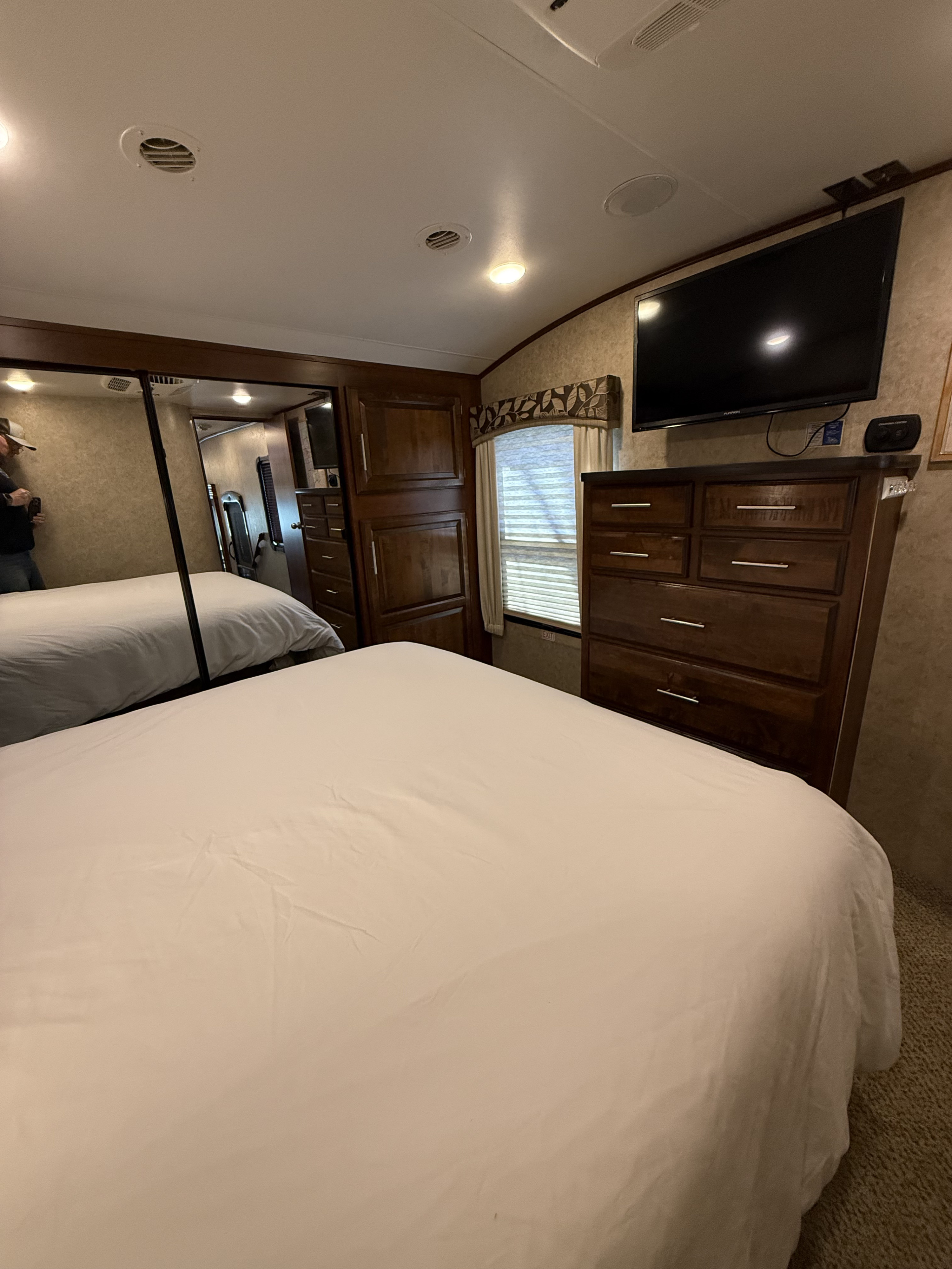 Comfortable RV rental bedroom featuring a large bed, wooden dresser, TV, and mirrored closet. Ideal for your travels.. Jayco Eagle 2017