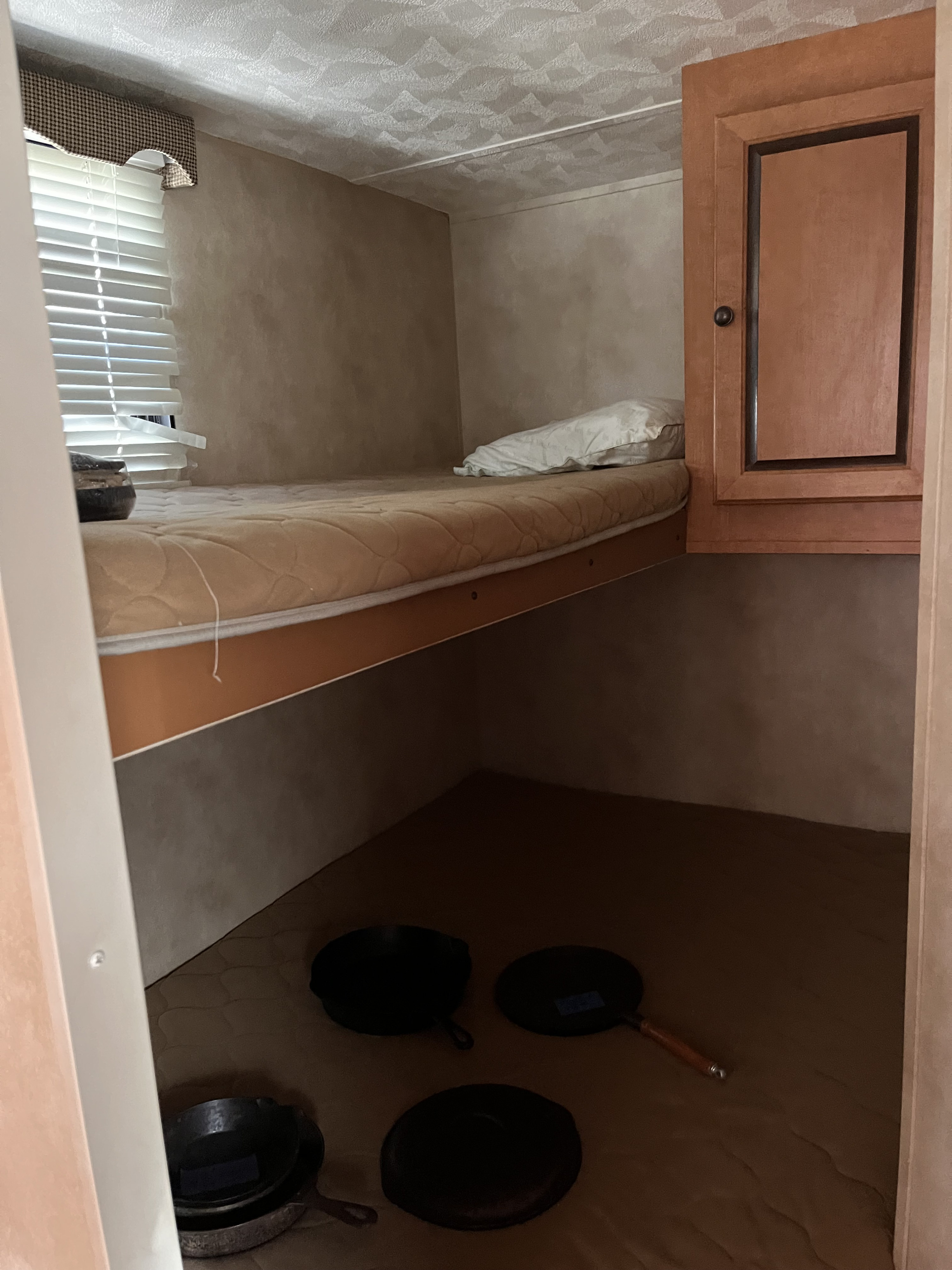 RV rental bunk bed with a window, wooden cabinet, and several cast iron pans on the floor below, inside a camper.. Forest River Palomino Canyon Cat 2014