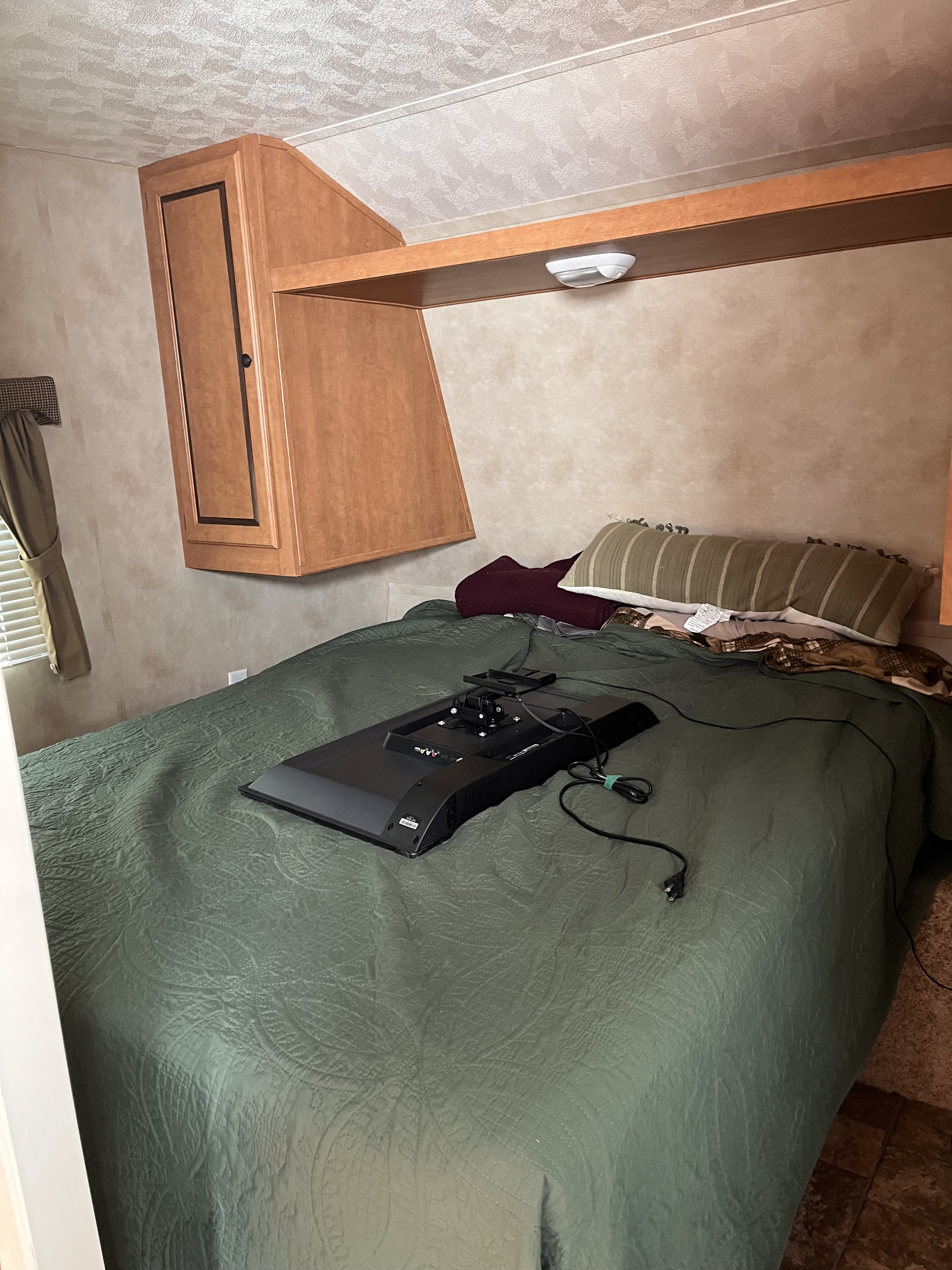 RV rental bedroom featuring a green bed, overhead cabinets, and a TV lying face down, ready for setup.. Forest River Palomino Canyon Cat 2014