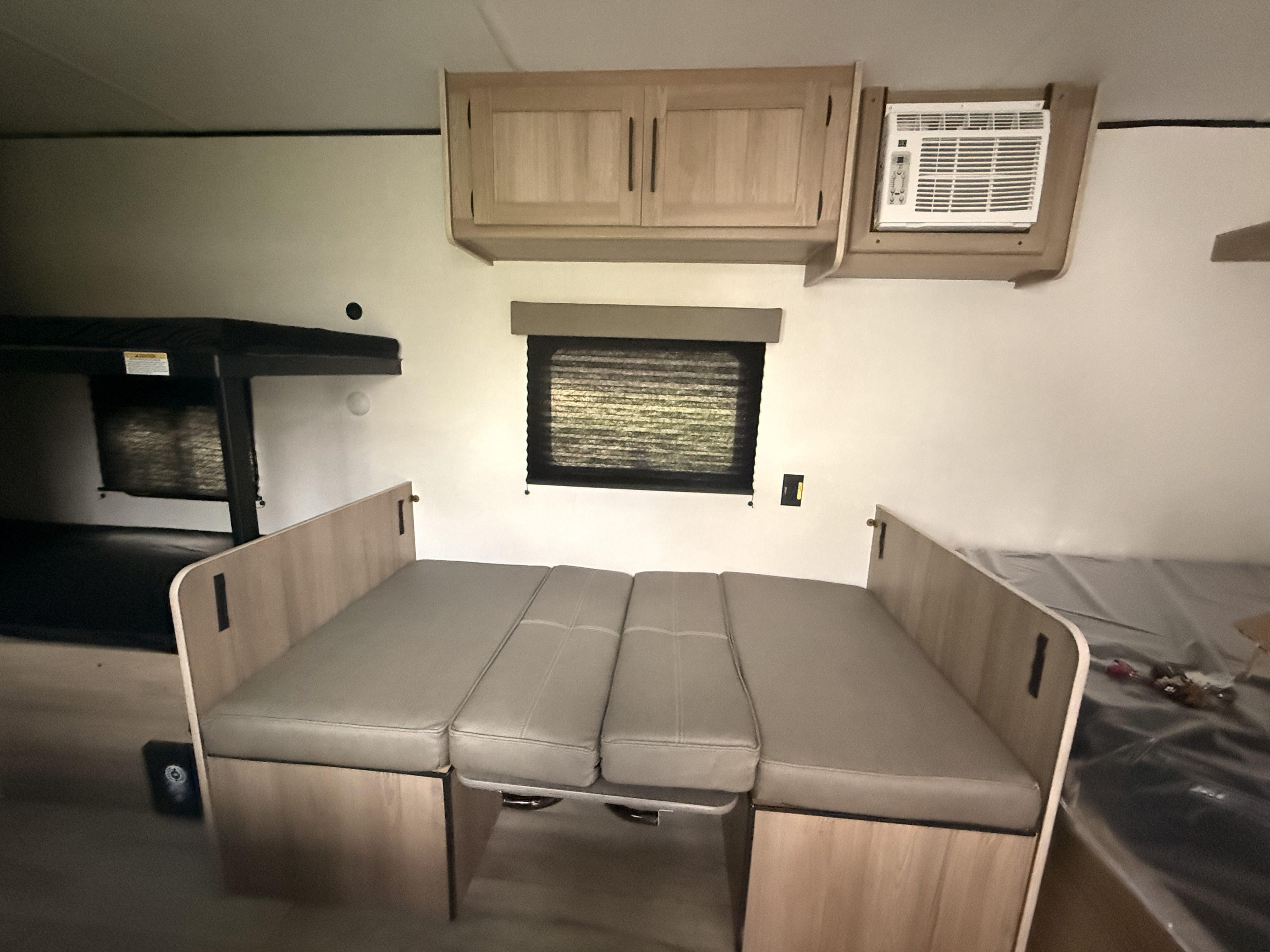 RV rental interior: bunk beds, convertible dinette with cushions, overhead storage, window, and wall-mounted AC unit.. Keystone Coleman 17B 2026