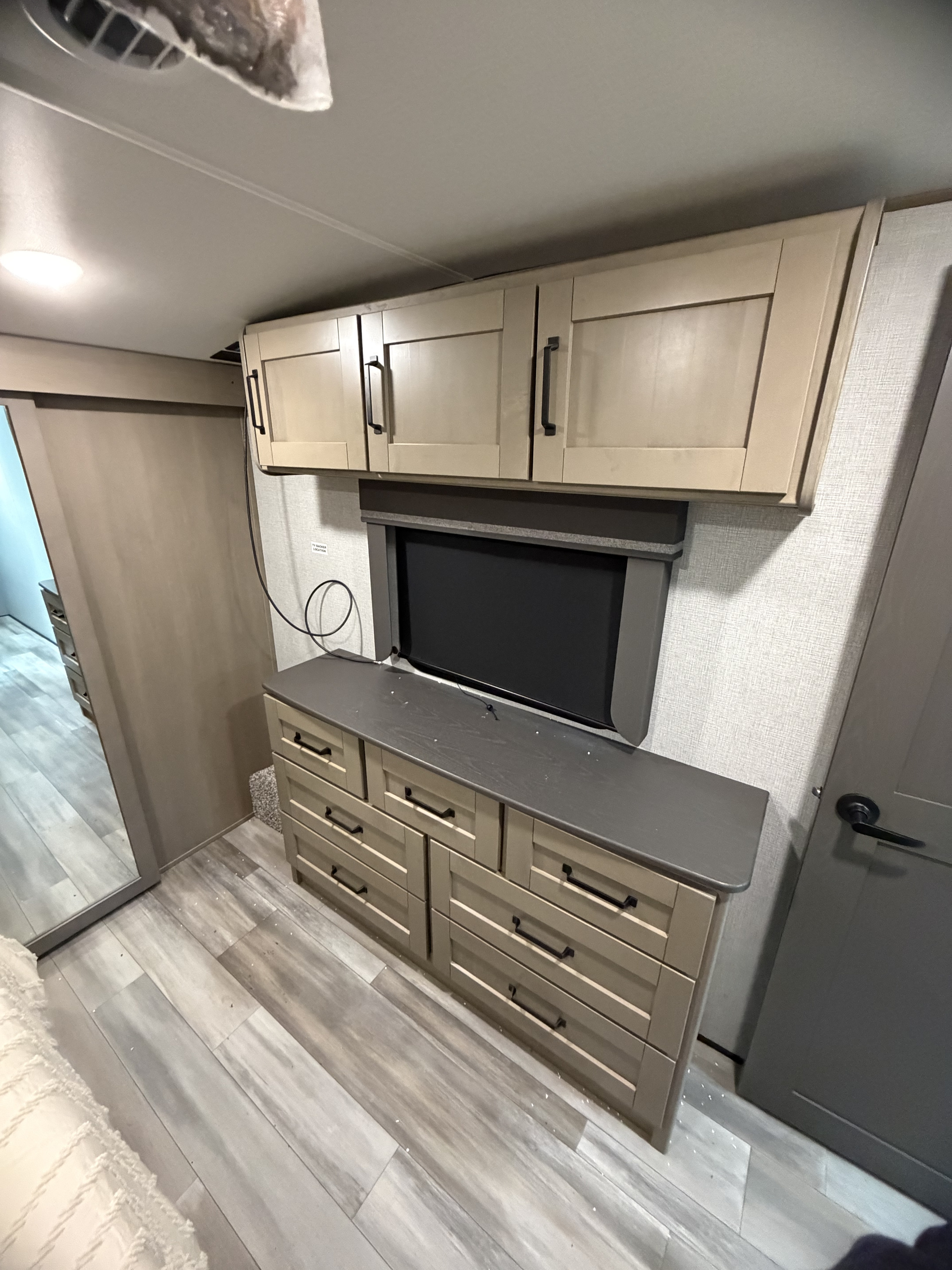 RV rental bedroom with light wood-toned dresser, overhead cabinets, recessed TV, and sliding closet door.. Grand Design Reflection 2023