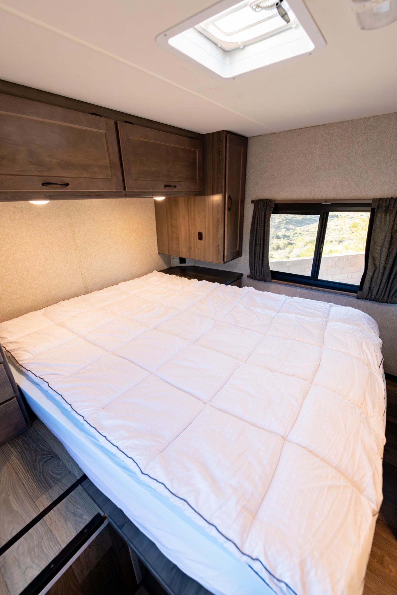 Cozy RV rental bedroom features a white bed, overhead cabinets, window view, and skylight. Ideal for travelers.. Winnebago Minnie Winnie 2020