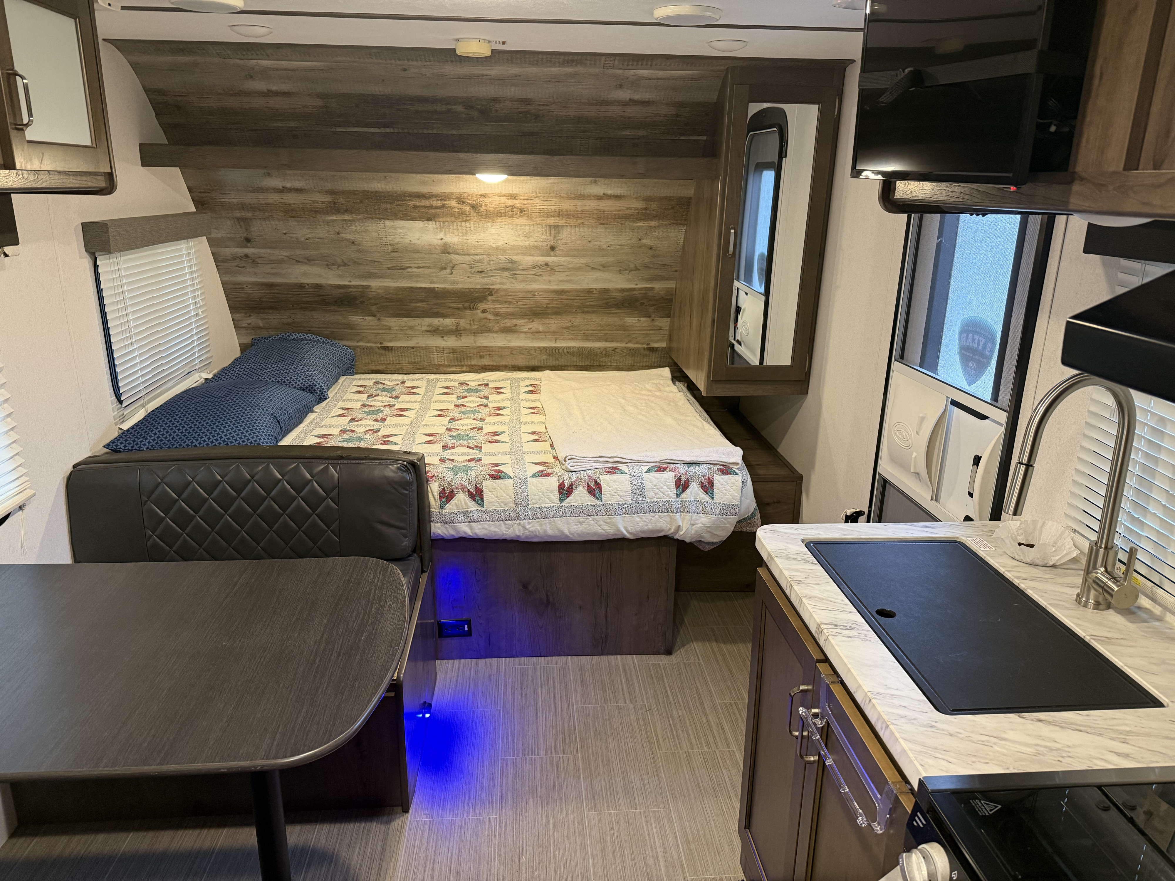 Inside this rv rental, a cozy bedroom with a quilt, a dinette, and a compact kitchen are visible in the well-lit interior.. Keystone RV Passport SL 2020