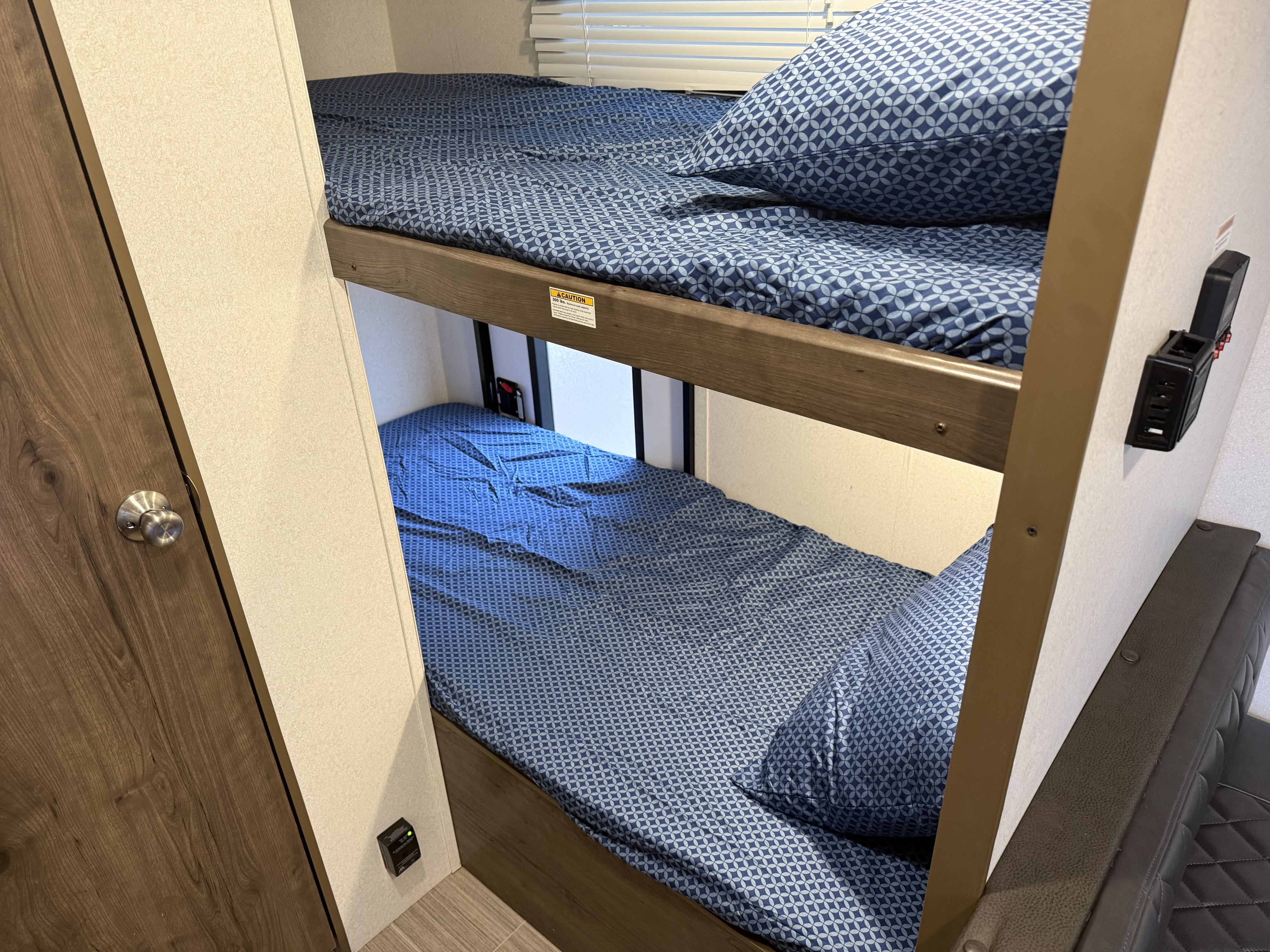 Inside an RV rental: blue patterned bunk beds, ready for a cozy night's sleep. Convenient outlets are visible.. Keystone RV Passport SL 2020