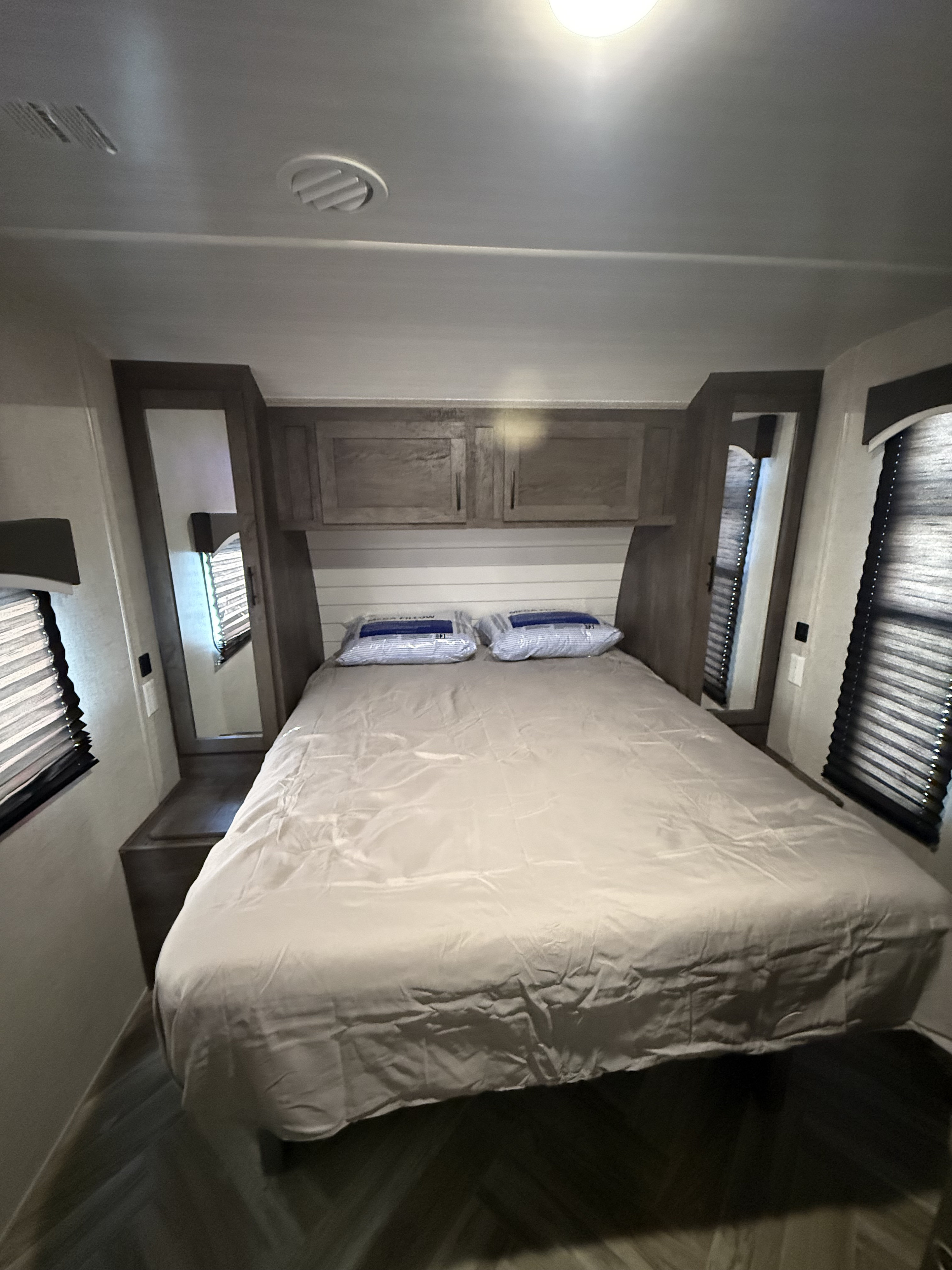 RV rental bedroom with a bed, two mirrors, overhead cabinets, and dual window blinds.. Forest River Evo 2021