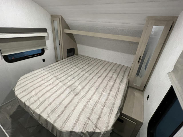 Cozy RV rental bedroom with a comfortable bed, window with blinds, and built-in storage. Ideal for travel accommodation.. Forest River Salem Cruise Lite 2023