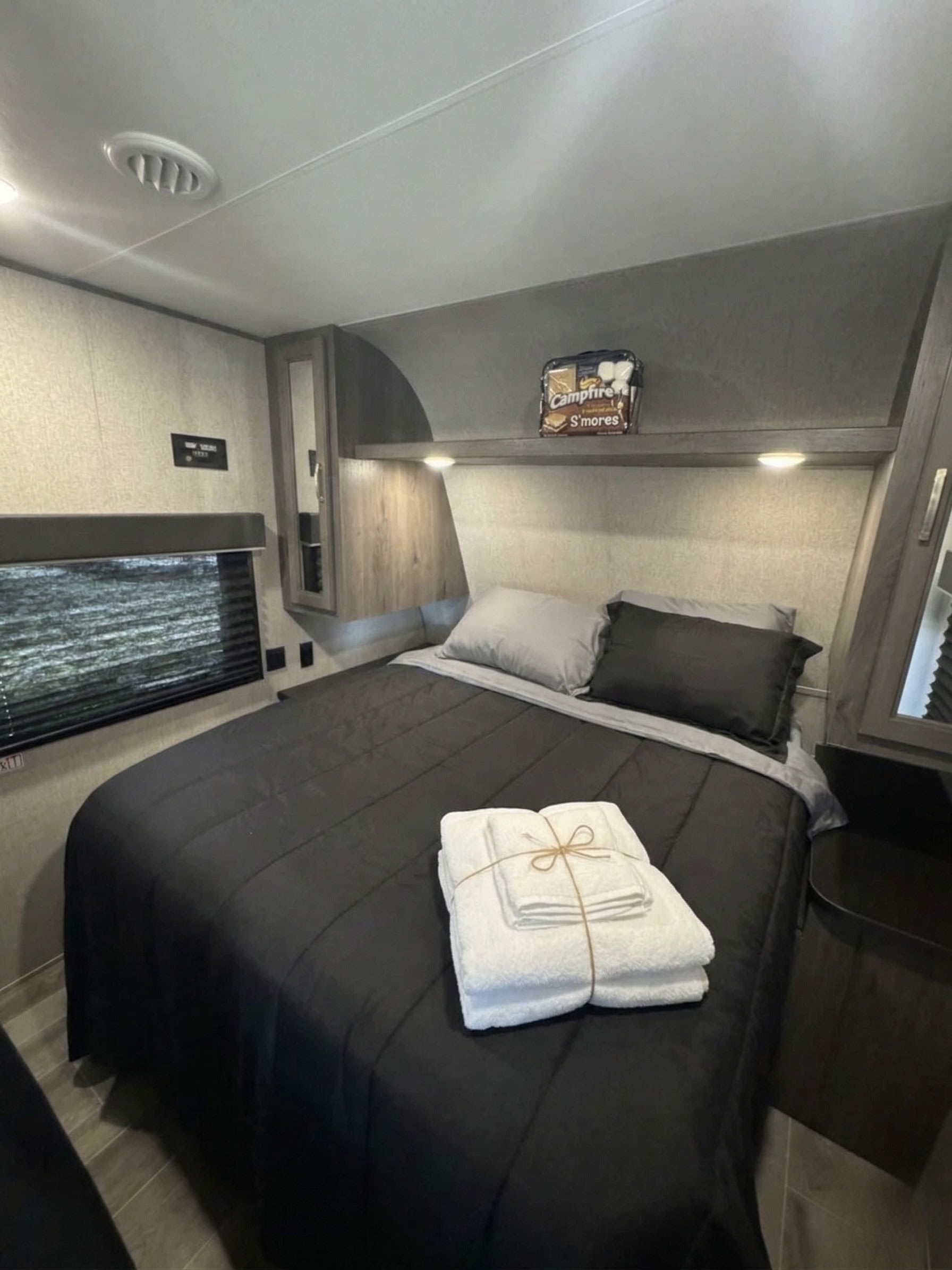 This cozy RV rental bedroom features a comfy bed with black comforter, grey pillows, fresh towels, and a S'mores kit for a cozy night.. Jayco Jay Flight SLX 2021