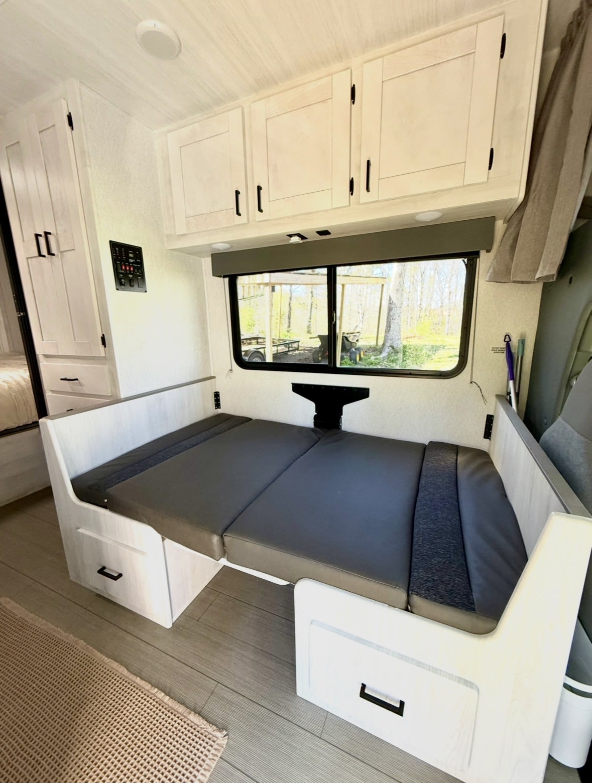 RV rental interior: Light wood dinette with gray cushions, overhead cabinets, and a window view, offering comfort and storage.. East to West Entrada 2024