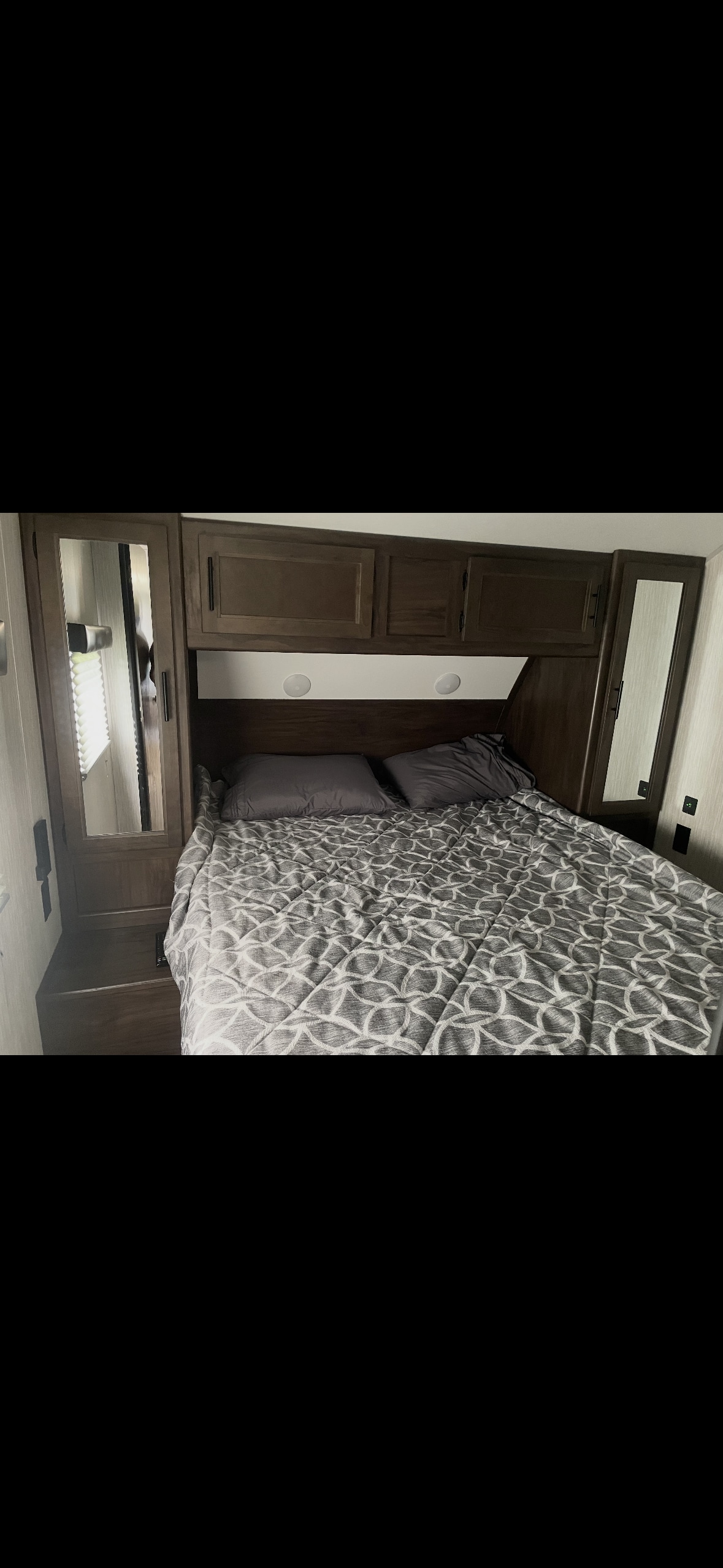 An RV rental bedroom featuring a bed with a gray patterned comforter, overhead cabinets, and mirrored wardrobes on each side.. Forest River Cherokee Grey Wolf 2021
