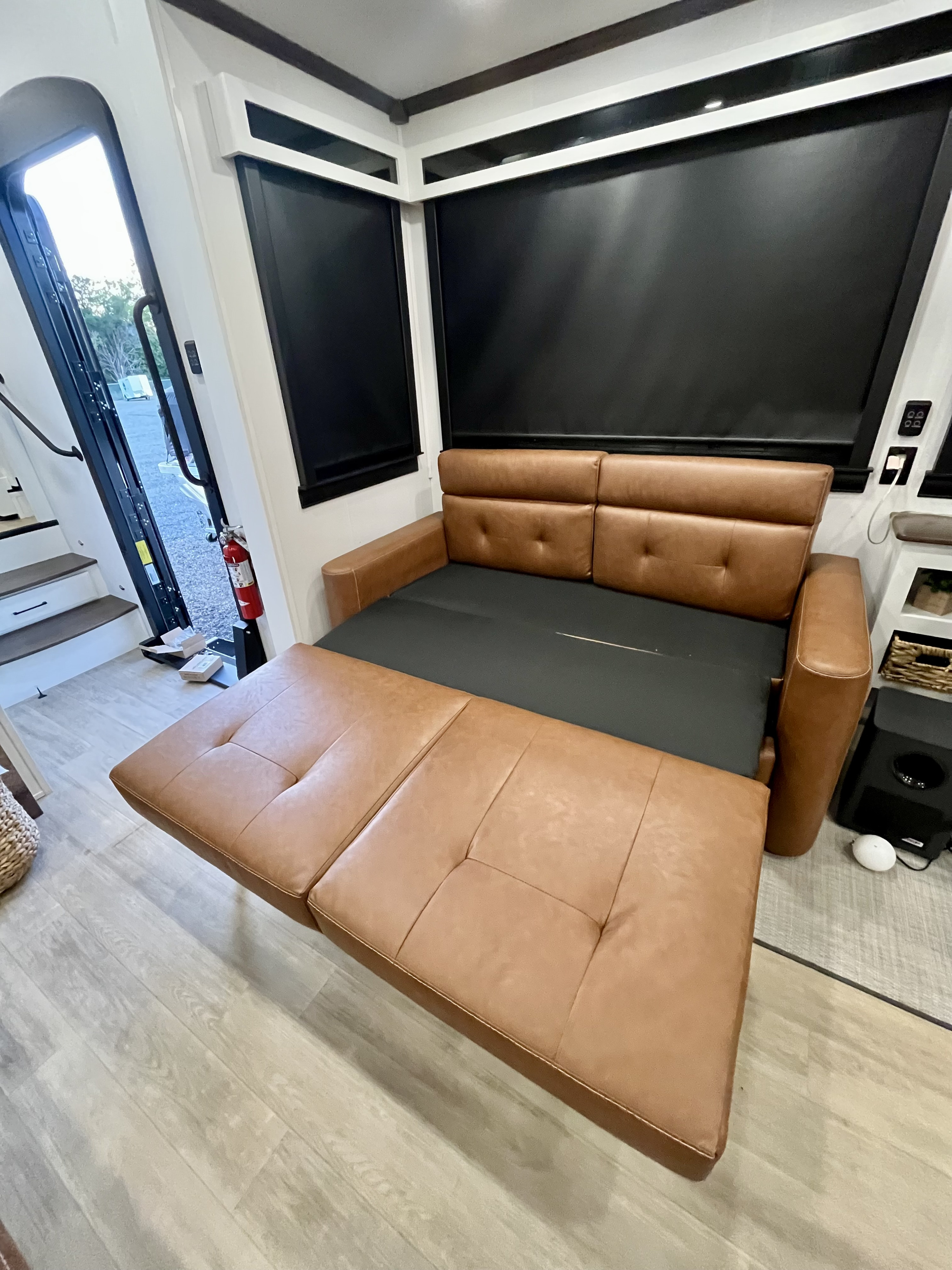 Inside this rv rental, a brown pull-out sofa bed is extended, revealing extra sleeping space near the entry door.. Forest River 39RKFB 2024