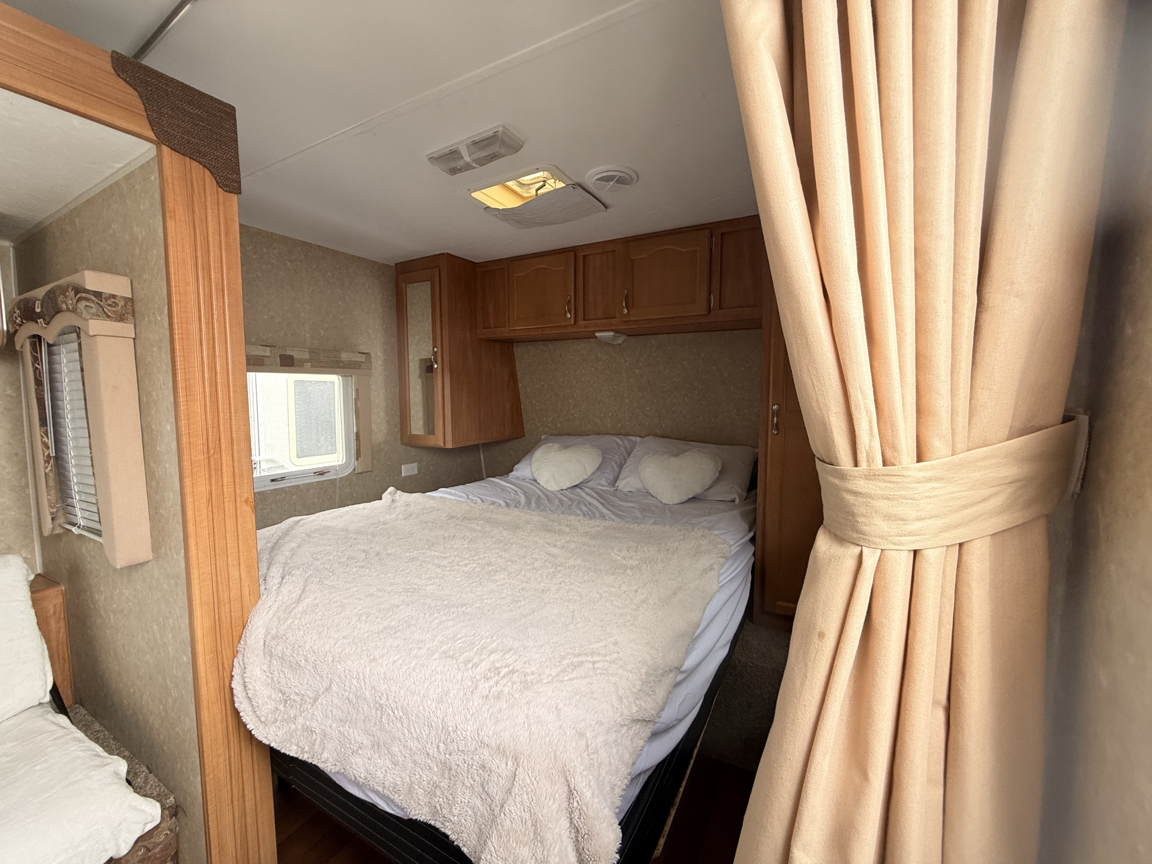 Cozy RV rental bedroom with a comfy bed, cabinets, and curtains. Ideal for a relaxing stay in your travel trailer.. Gulf Stream Conquest 2009