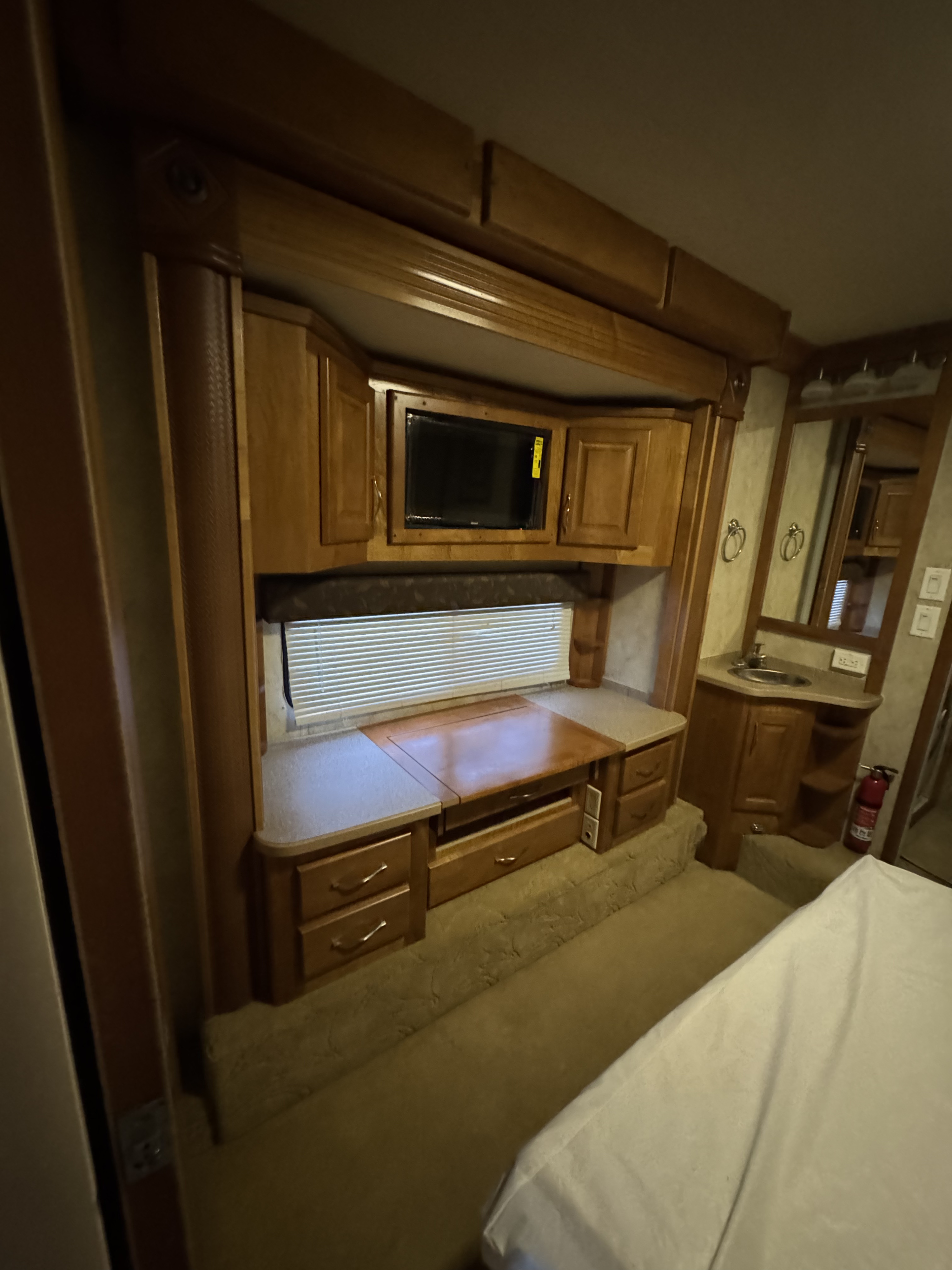 Inside this rv rental: cozy bedroom featuring rich wood cabinetry, built-in TV, desk area with window, and a compact sink vanity.. Gulf Stream Tour Master 2007