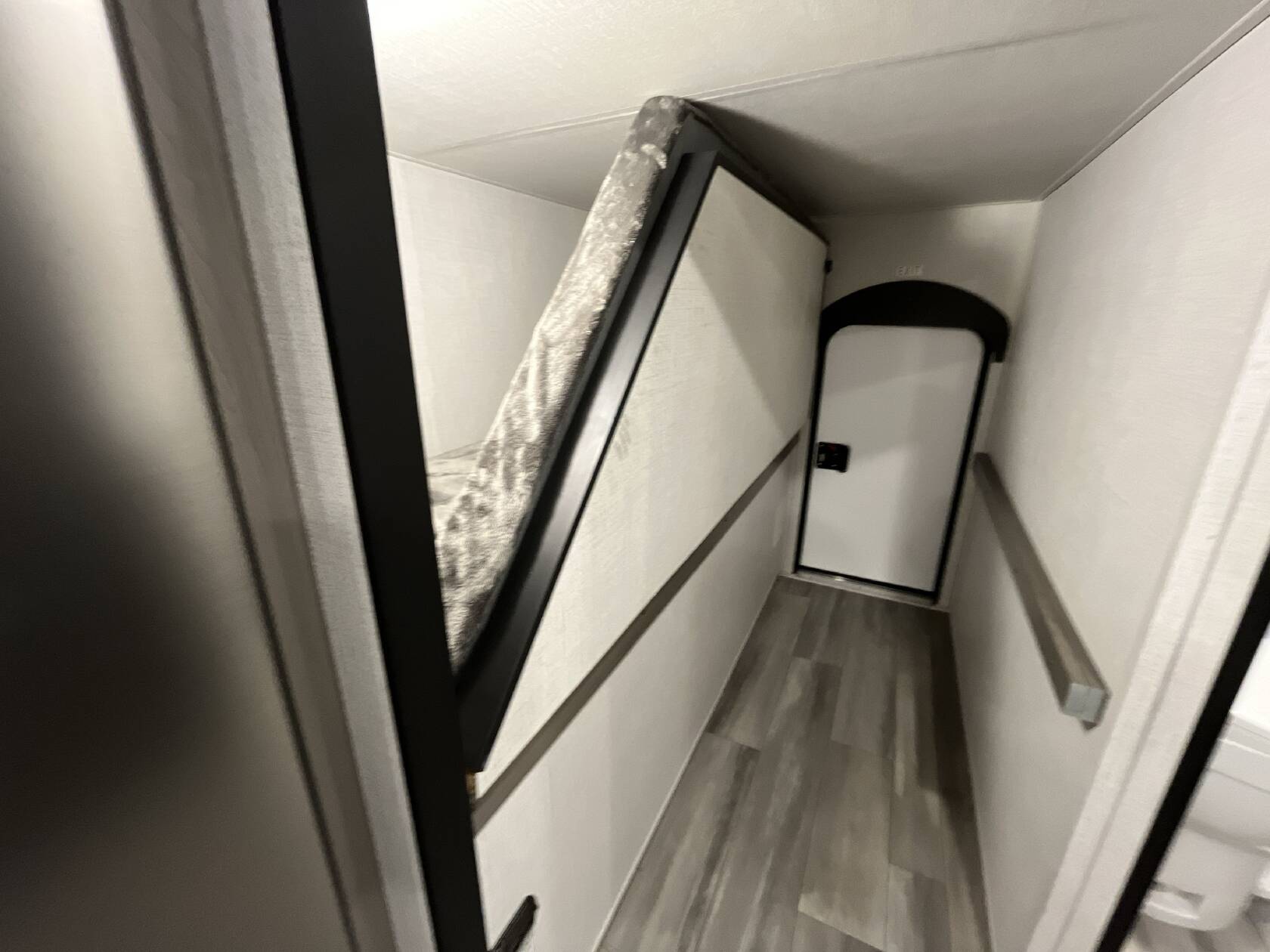Inside an rv rental: a compact hallway with an angled bunk bed on the left, leading to an exit door with a light above. Laminate floor.. Keystone RV Hideout Sport 2024