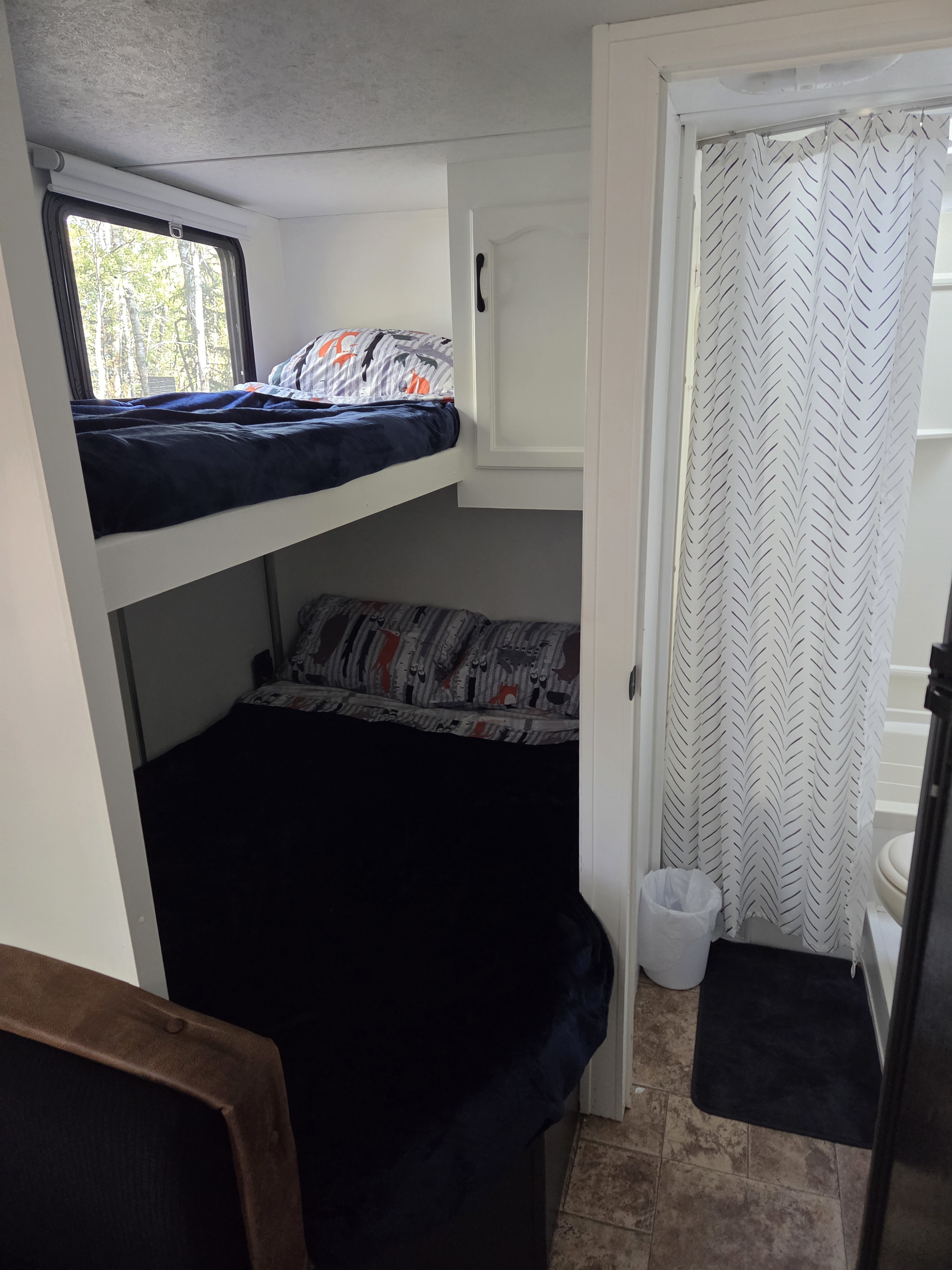 Cozy RV rental interior with bunk beds, patterned bedding, and a compact bathroom featuring a white chevron shower curtain.. Keystone RV Springdale 2011