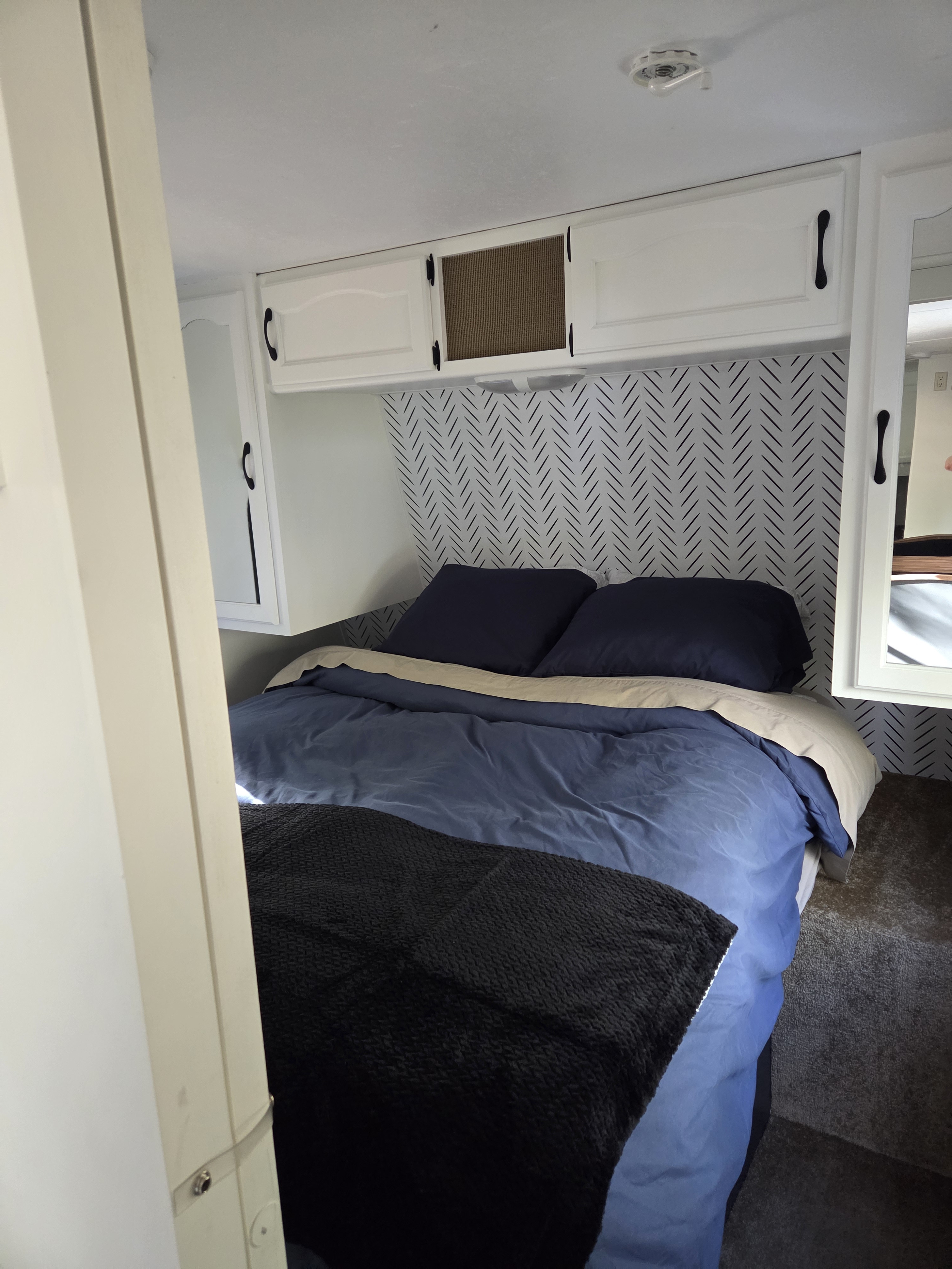 Experience comfort in this RV rental bedroom: blue bedding, black throw, herringbone accent wall, and white overhead storage.. Keystone RV Springdale 2011