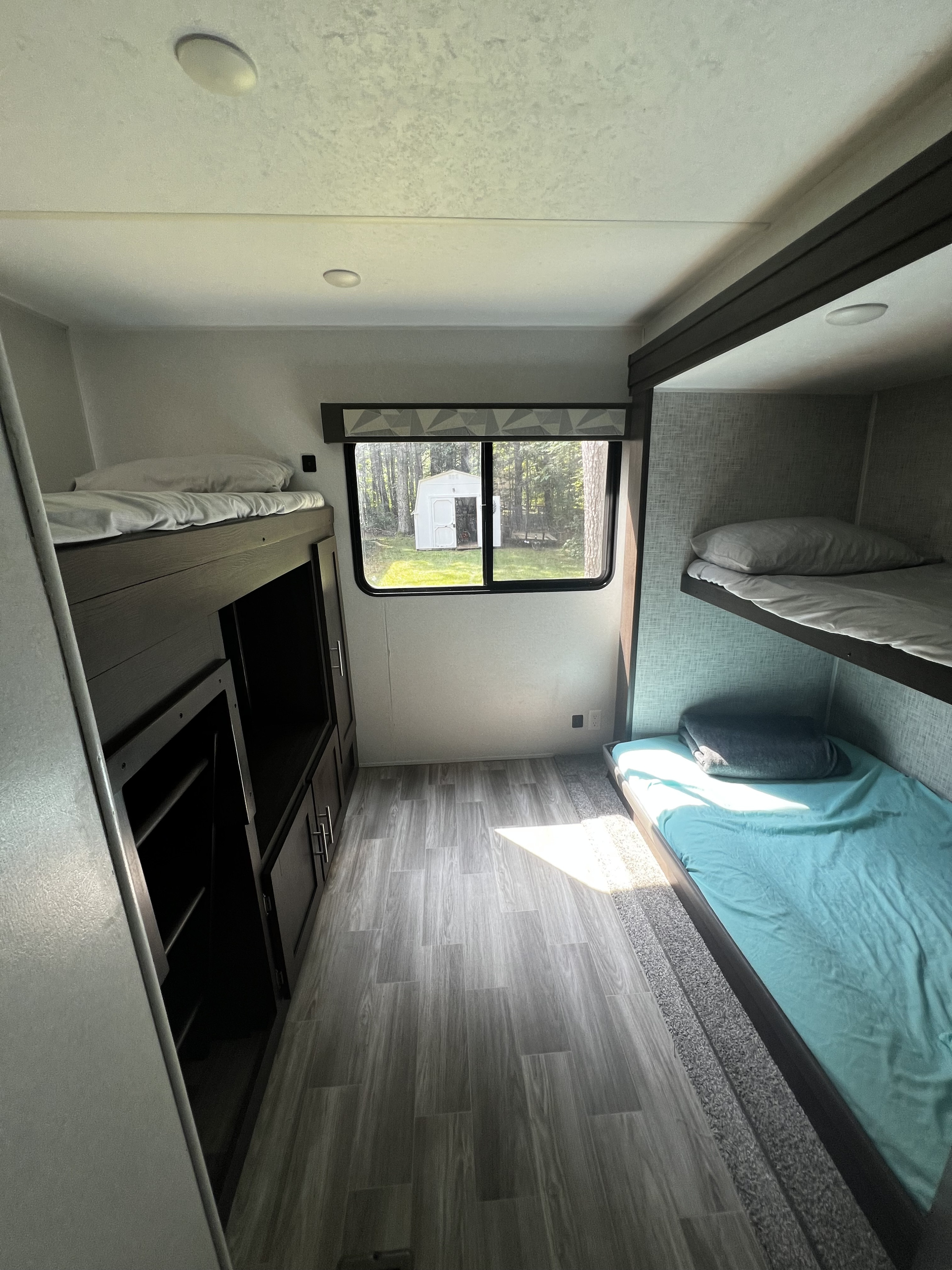 Inside an RV rental: a bright bunkhouse with comfortable beds, storage, and a view of nature outside the window.. Forest River Wildwood 2020