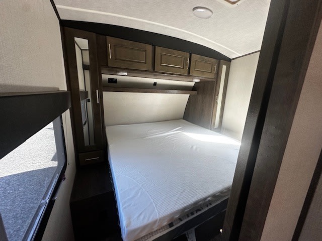 Spacious rv rental bedroom with a comfortable queen bed, dark wood cabinets, and a mirrored wardrobe. Natural light enters from a side window.. Heartland RVs Torque Toy Hauler 2019