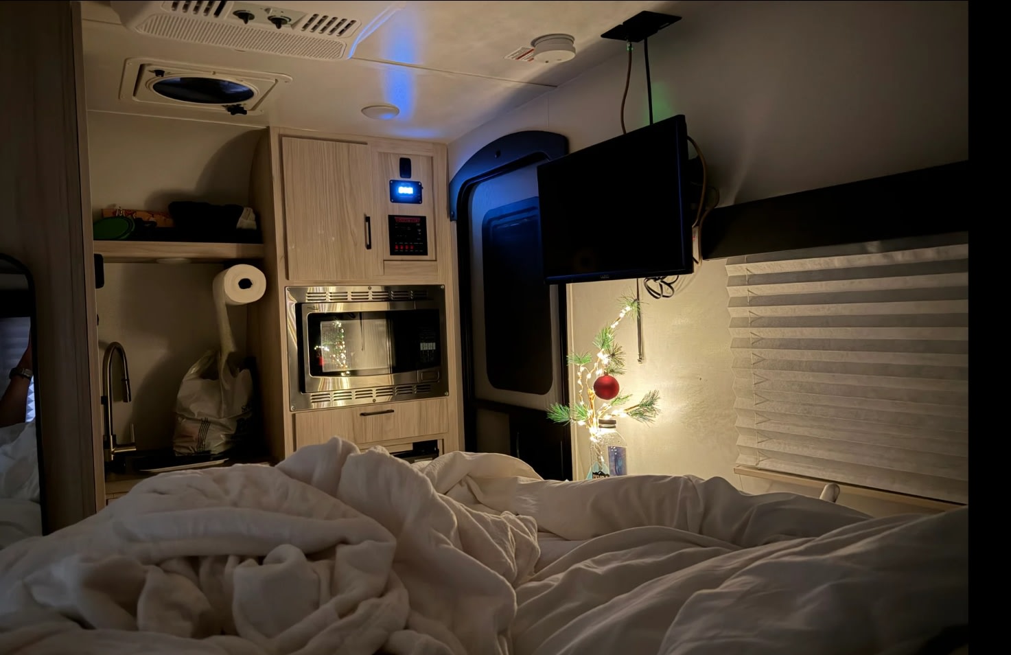 Inside a cozy RV rental: a warm bed in the foreground, a compact kitchen with a microwave, and a festive mini tree by the window.. Winnebago Hike 100 2023
