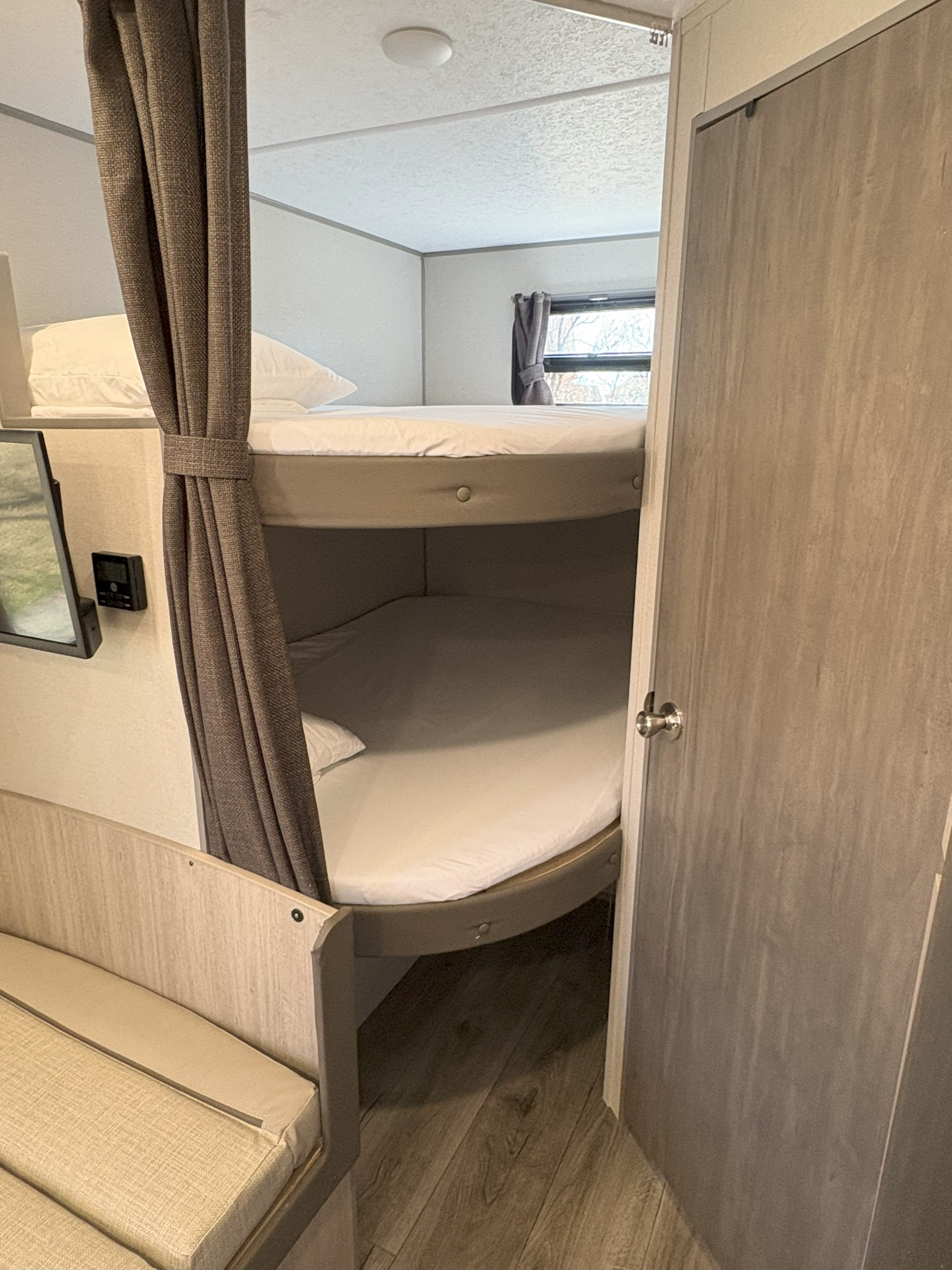 Cozy bunk beds in an RV rental, featuring privacy curtains, white bedding, a window, and a small screen. Perfect for families.. Coachmen Coachmen Catalina Summit 2025