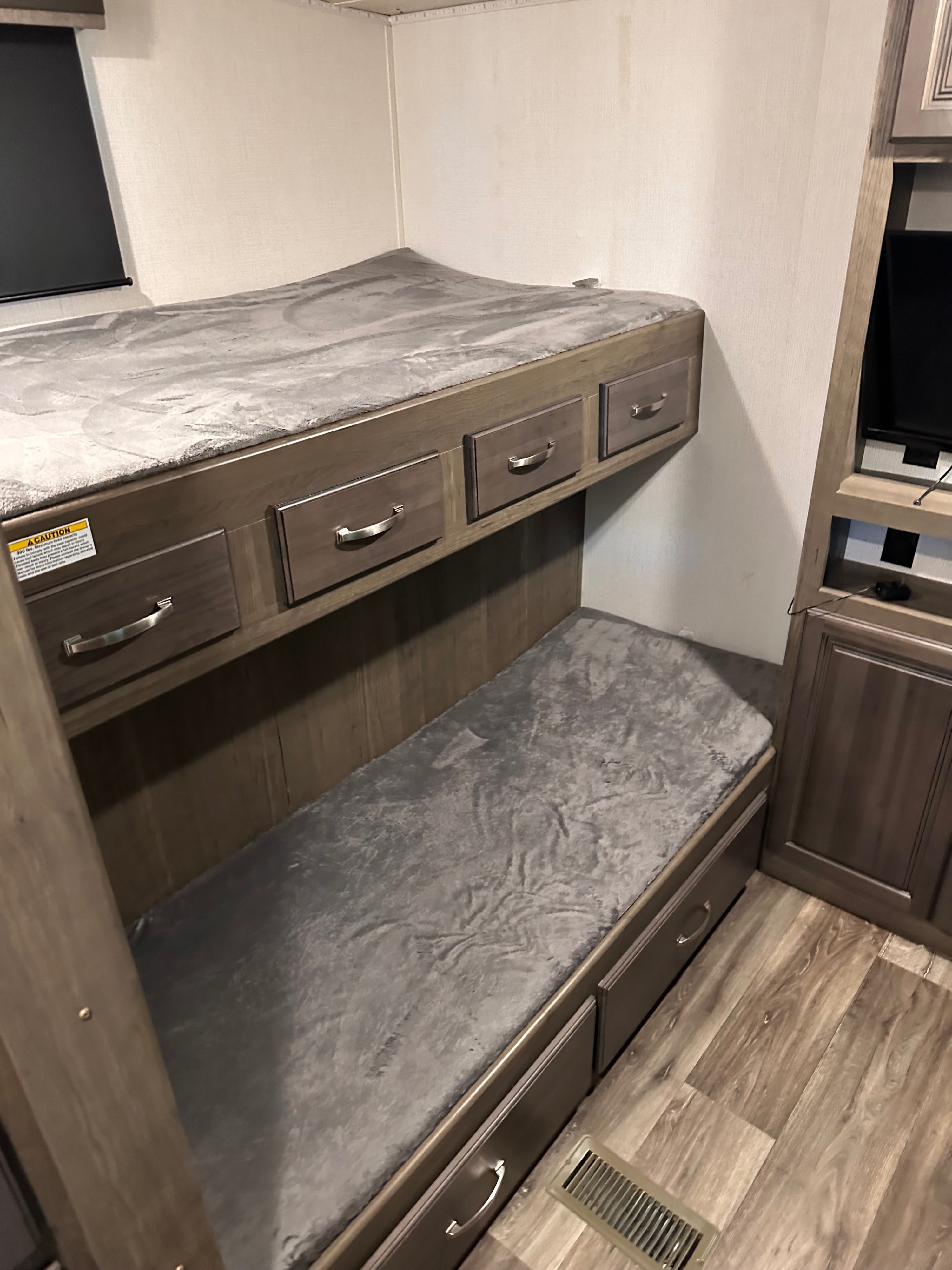 Cozy RV rental bunk beds, top and bottom, with soft grey bedding and integrated storage drawers.. Keystone RV Cougar 2022