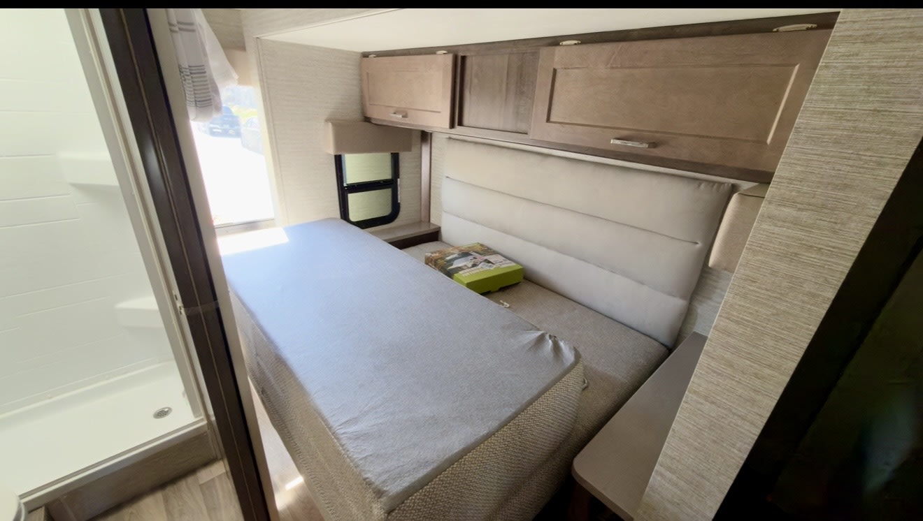 Explore this RV rental's compact interior: a bed with overhead cabinets, and a convenient adjacent shower.. Winnebago Spirit 2021