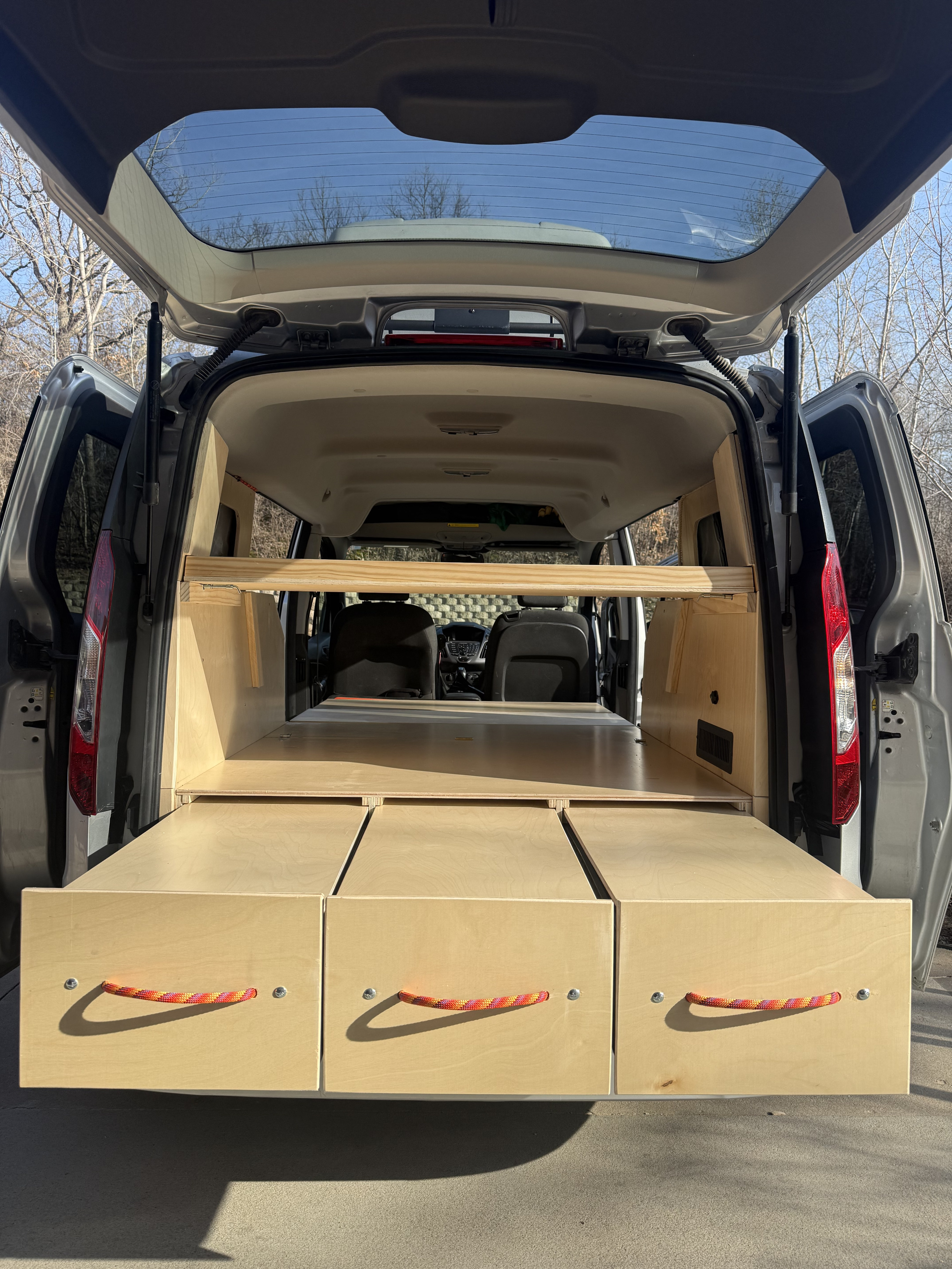 RV rental van with a custom wooden interior, showing pull-out drawers and a bed platform. The back is open to the outdoors.. Ford Transit custom 2015