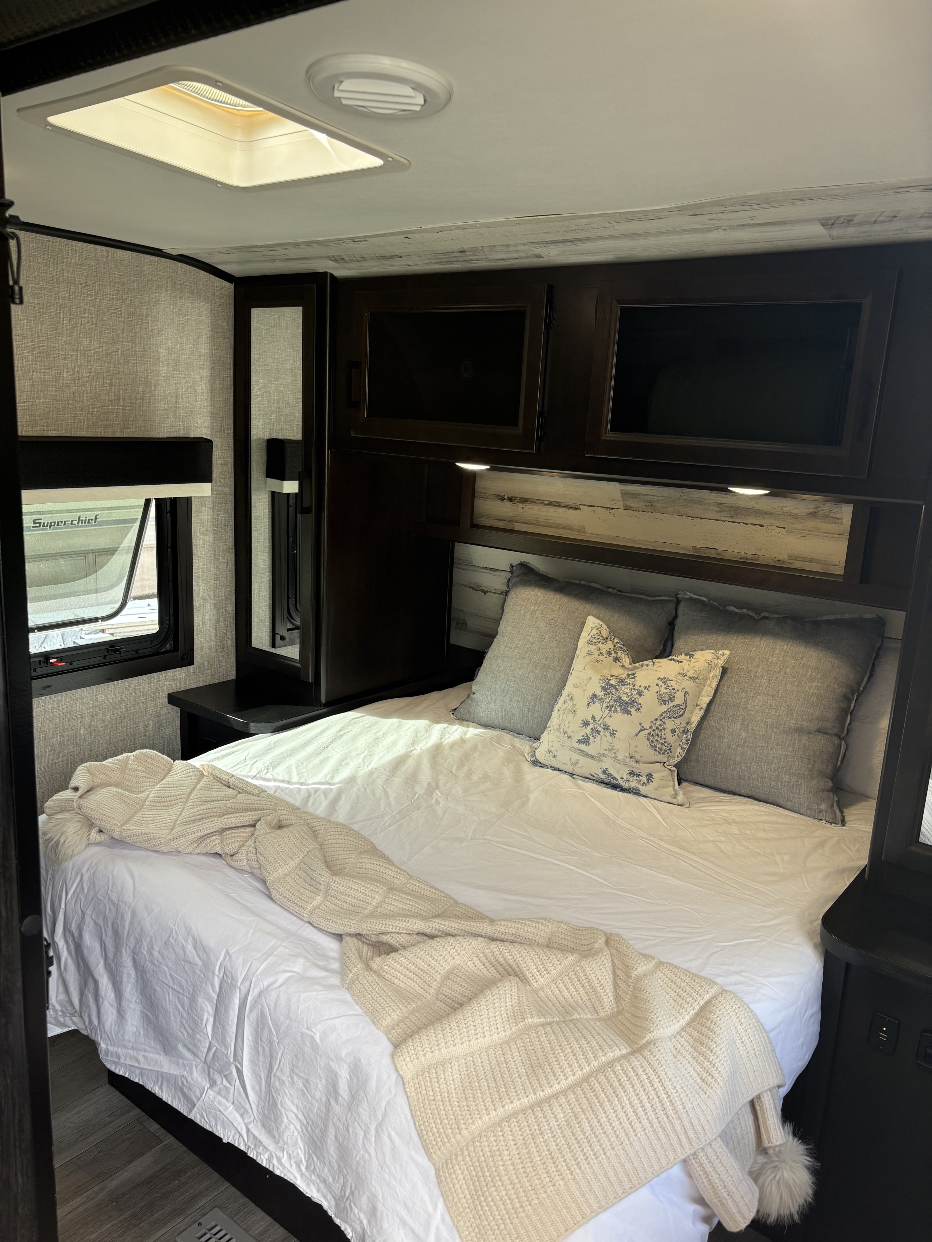 Modern RV rental bedroom featuring a comfy bed, dark wood cabinets, and skylight. Enjoy cozy travels!. Jayco Jay Feather 2022