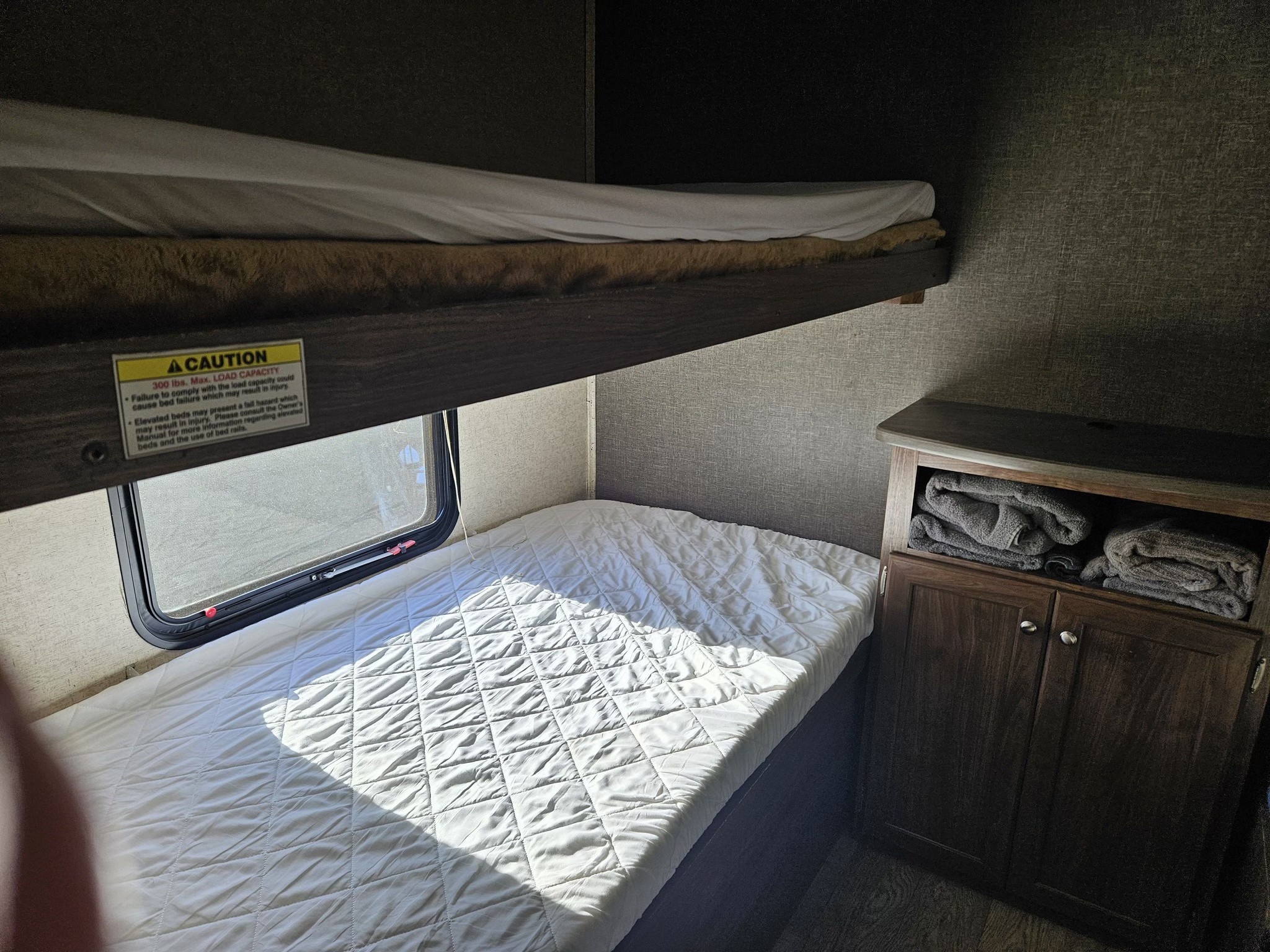 RV rental featuring bunk beds, a window, and storage. Upper bed has a 300 lbs max load capacity warning.. Heartland RVs Prowler 2018