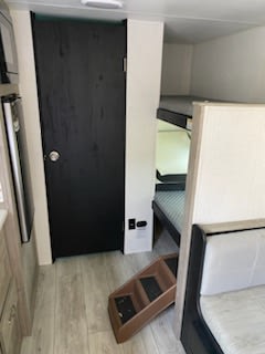 This RV rental's interior features cozy bunk beds, a black door (likely a bathroom), and a partial view of a compact kitchen area.. Heartland RVs Trail Runner 2024
