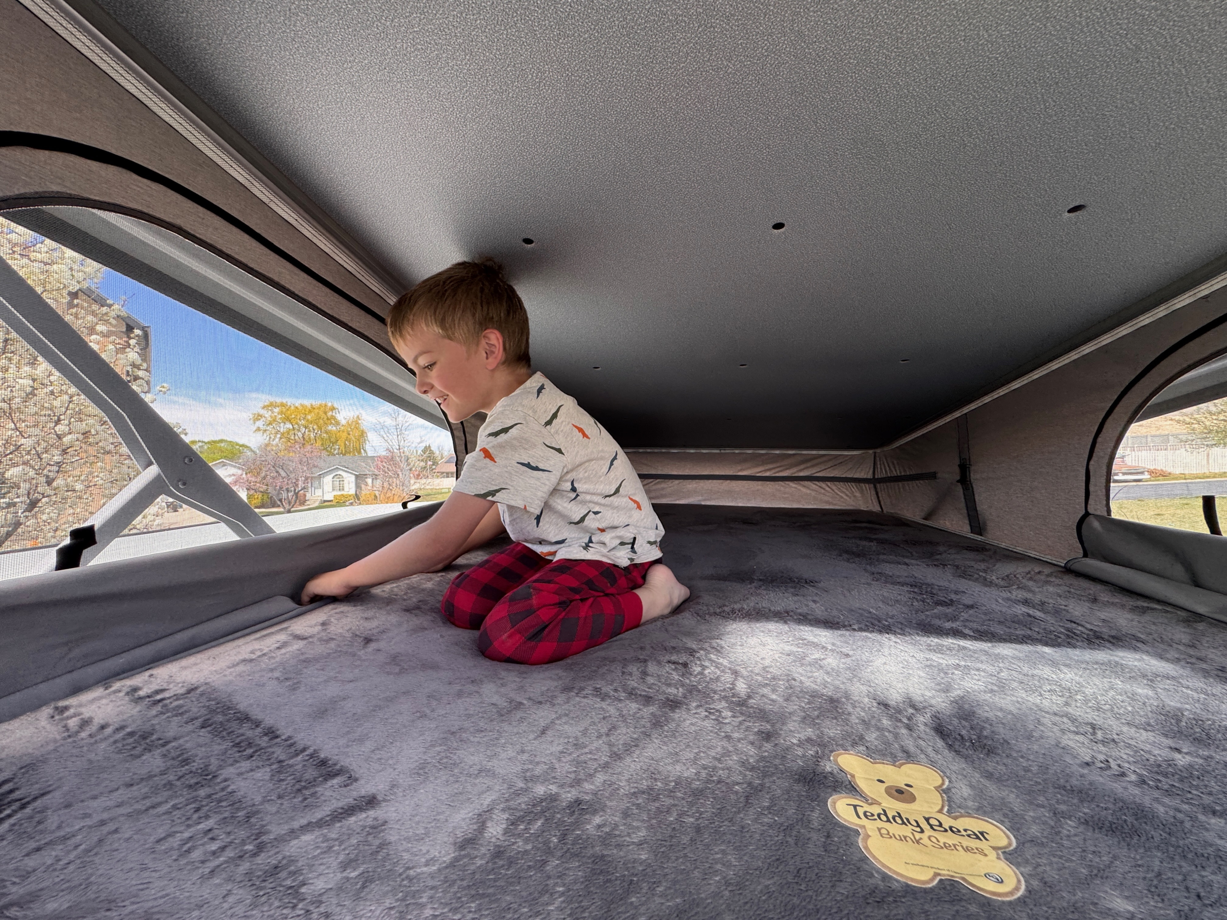 A happy child explores the cozy pop-top bunk in an RV rental, gazing out at nature. Perfect for family camping adventures!. Forest River Coachmen Nova 2026