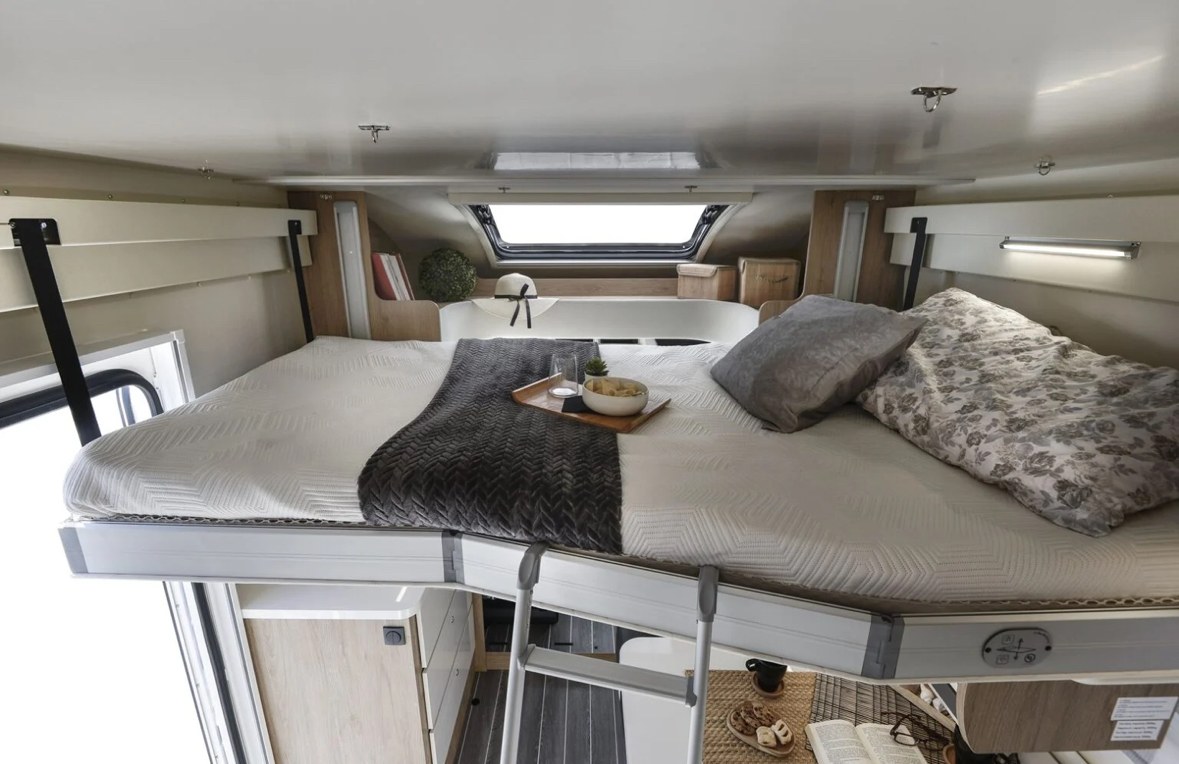 Cozy overhead sleeping area in an RV rental, complete with a made bed, breakfast tray, and ladder for access.. Ford Rollerteam 747 2026