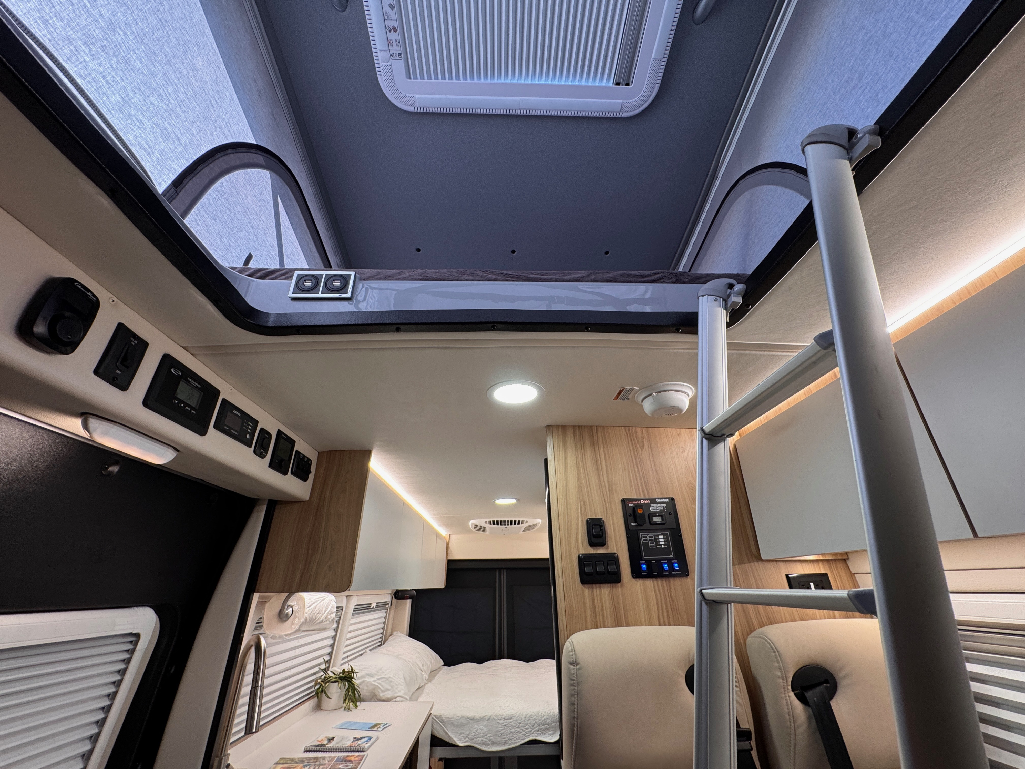 Spacious rv rental interior featuring a raised pop-top roof, ladder to an upper bed, rear bed, control panels, and bright lighting.. Forest River Coachmen Pixel 2026