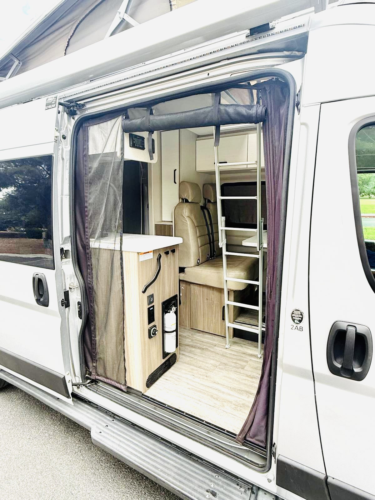 Open RV rental camper van showing interior with compact kitchen, seating, and a ladder to an upper bunk bed.. Thor Dazzle 2024