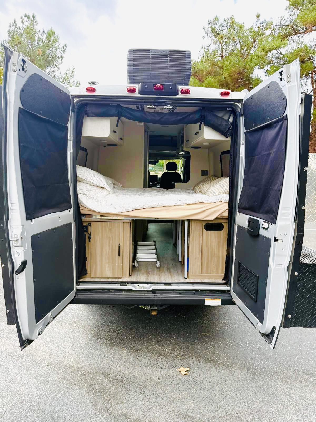 Step inside this cozy RV rental camper van, featuring a comfortable bed, convenient storage, and open back doors.. Thor Dazzle 2024