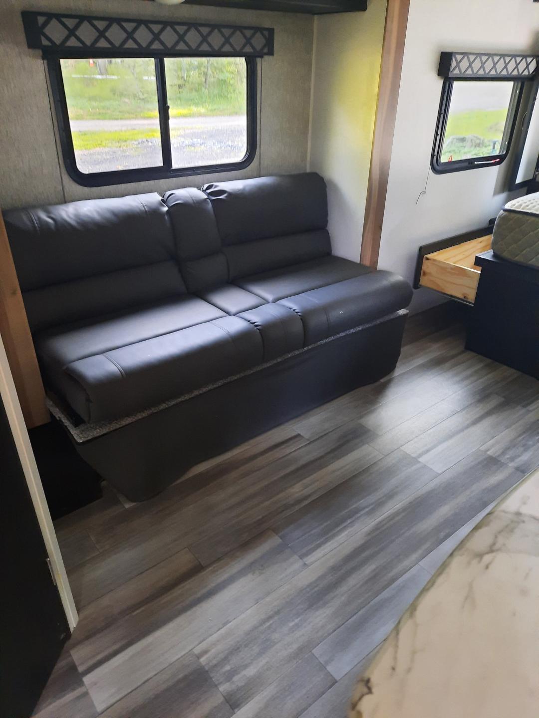 RV rental interior features a dark upholstered sofa, large windows, wood-look flooring, and storage. Cozy and functional.. Forest River Coachmen Freedom Express Ultra Lite 2022