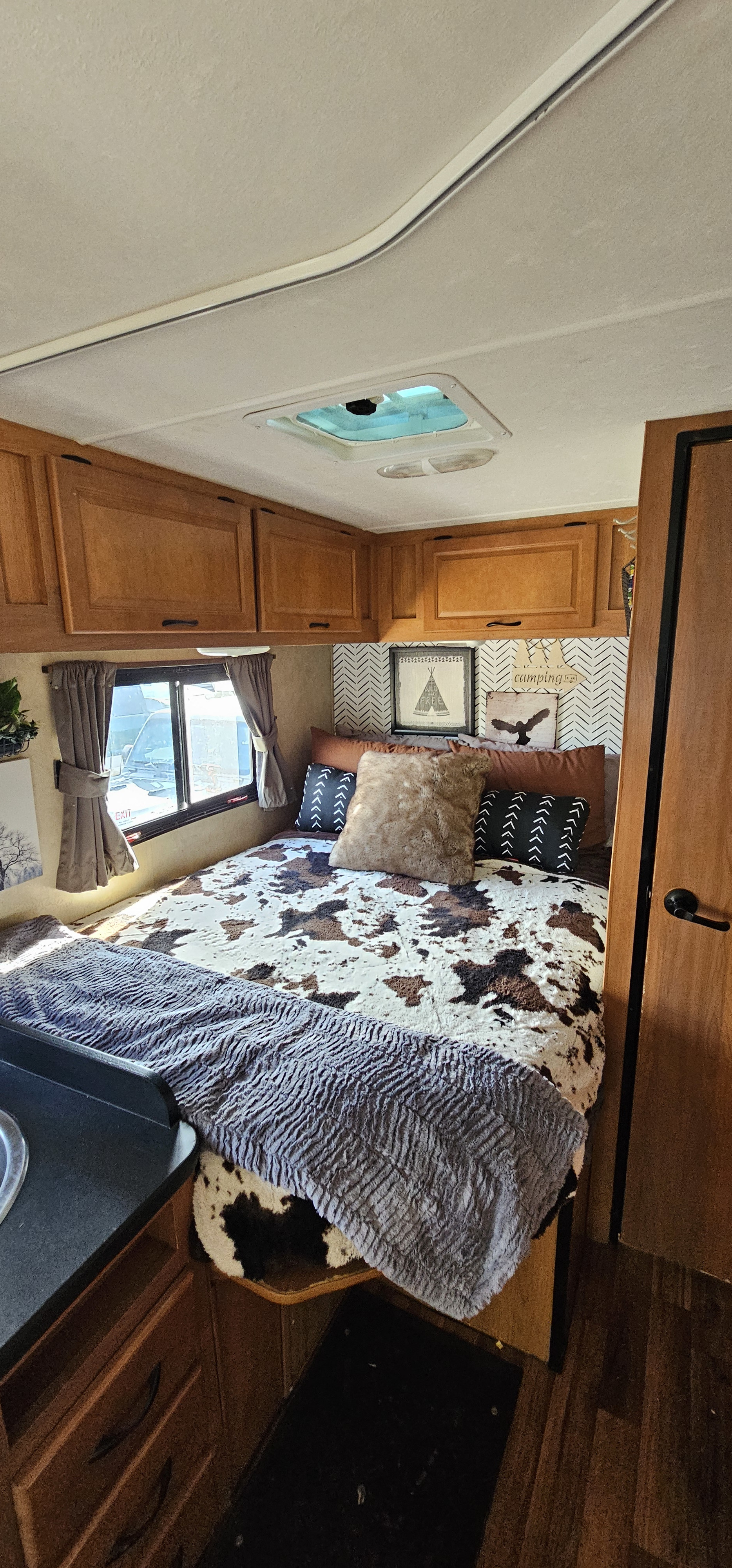 This cozy RV rental bedroom features a cowhide bed, overhead cabinets, and nature-inspired decor, perfect for glamping.. Thor Majestic 2014
