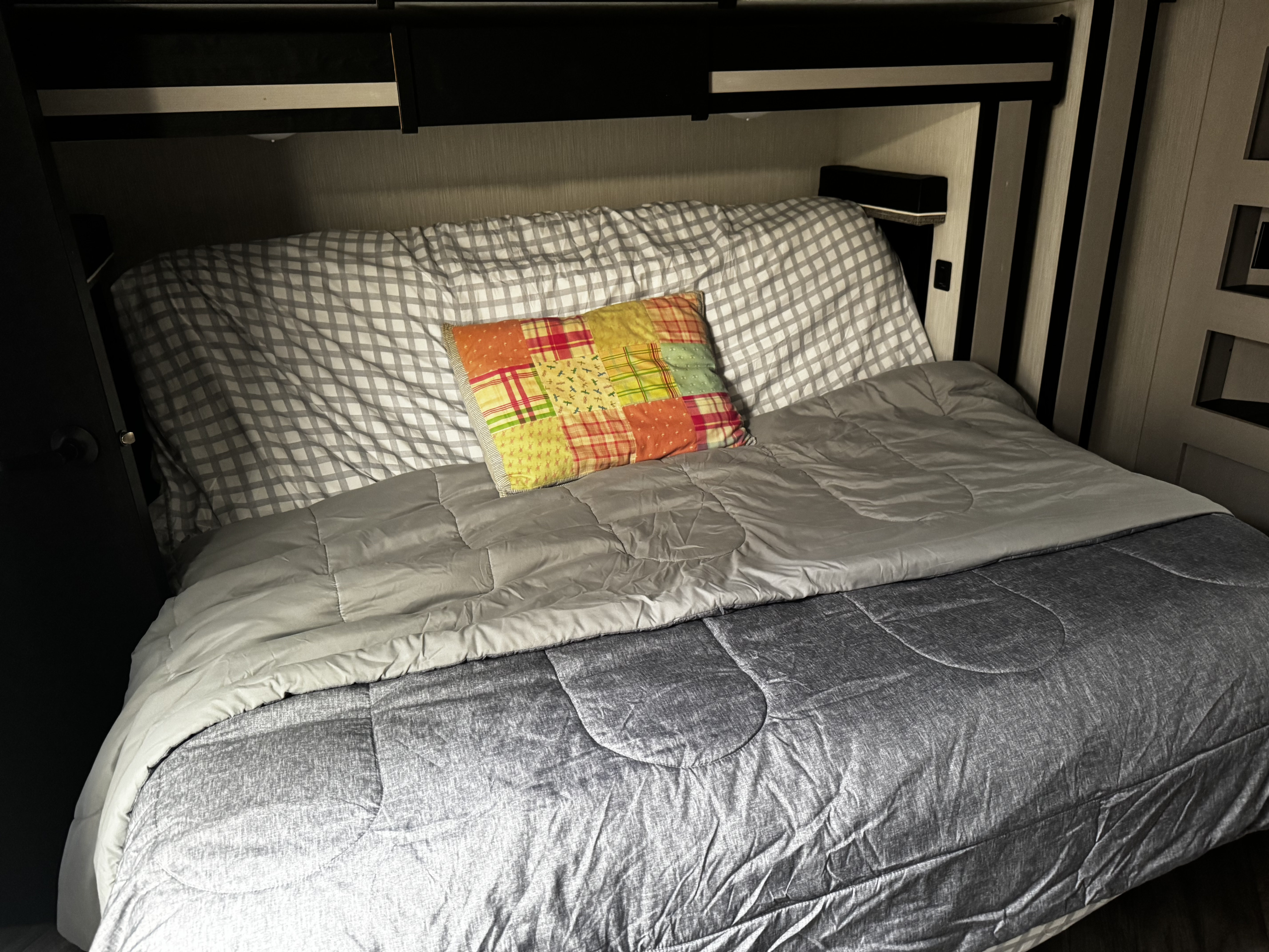 Cozy RV rental bed with checkered sheets, a patchwork pillow, and grey comforters. Perfect for comfortable travel.. Heartland Cyclone 2022