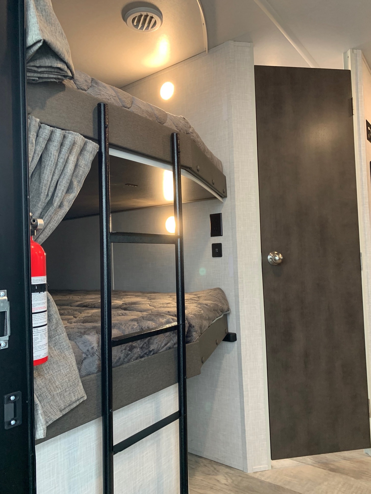 Inside an RV rental: view of bunk beds with ladder, curtains, fire extinguisher, and interior door for guests.. Forest River Rockwood Ultra Lite 2021