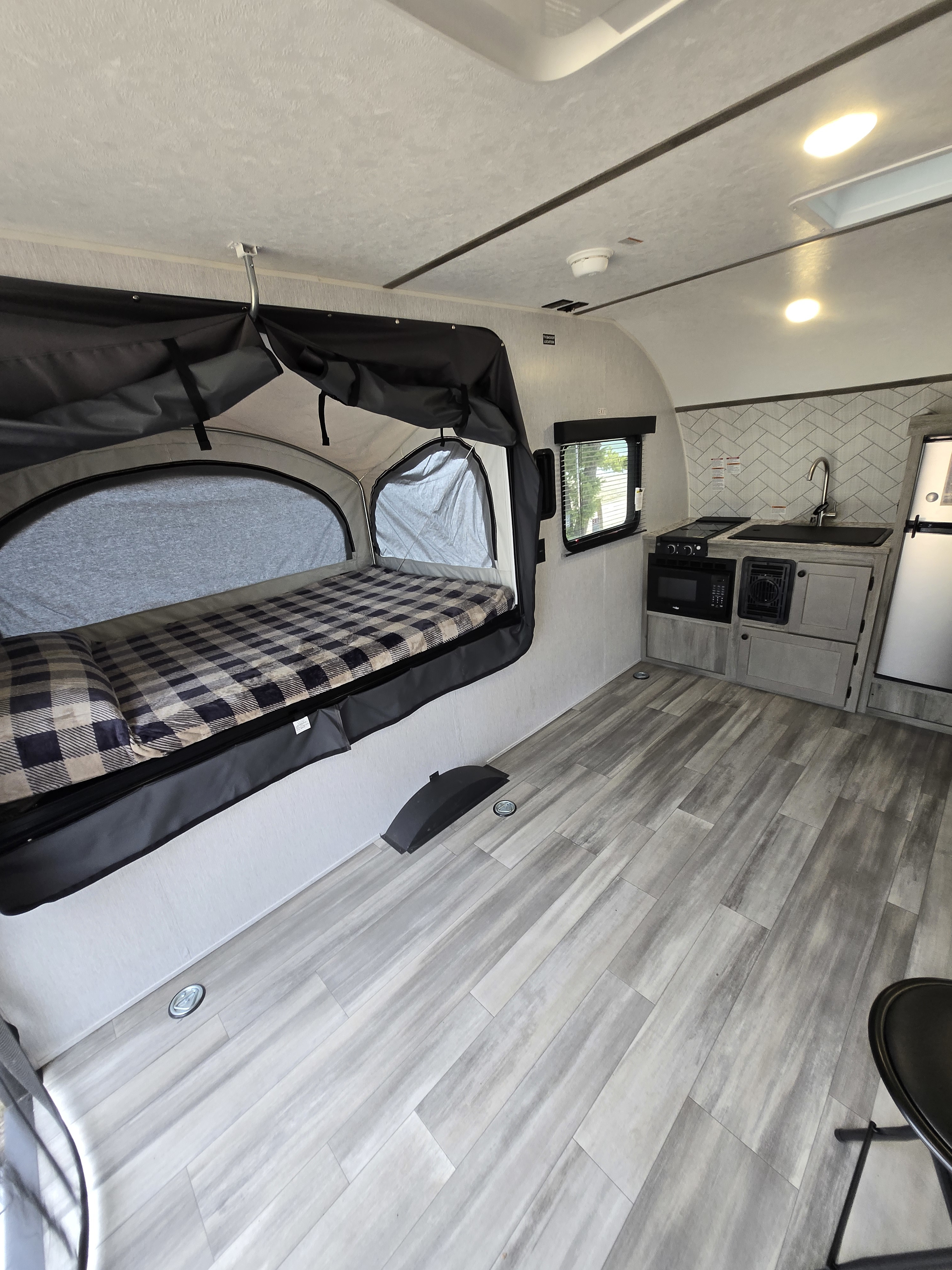 Compact RV rental interior: pop-out bed with plaid blanket, kitchenette with sink & stove, and wood-look flooring.. Wayfinder Go Lite Boulderback TH 2026