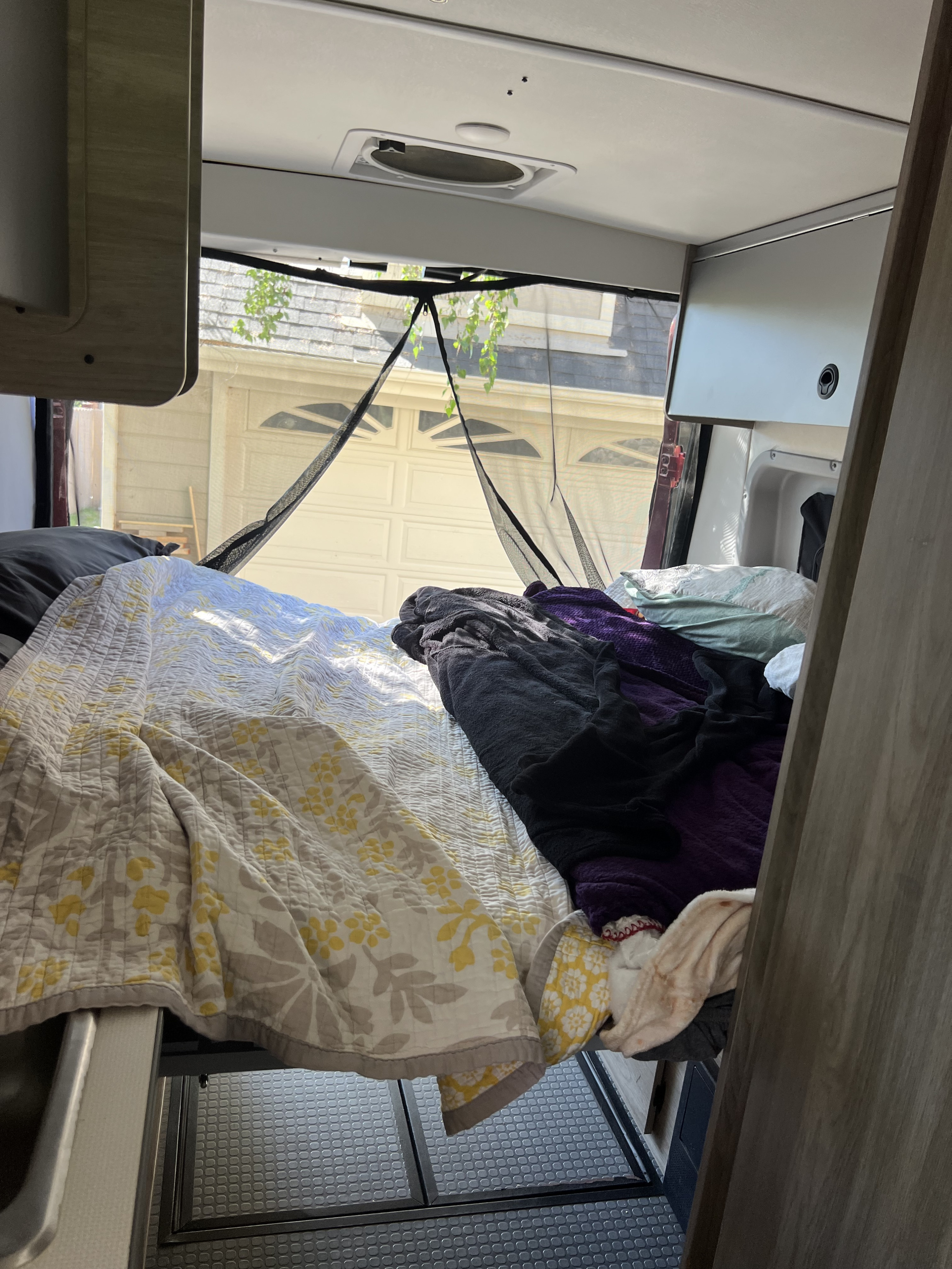 Relaxing rv rental bedroom with bed, blankets, ceiling vent, and a screened view of a garage outside.. Winnebago Solis 2022