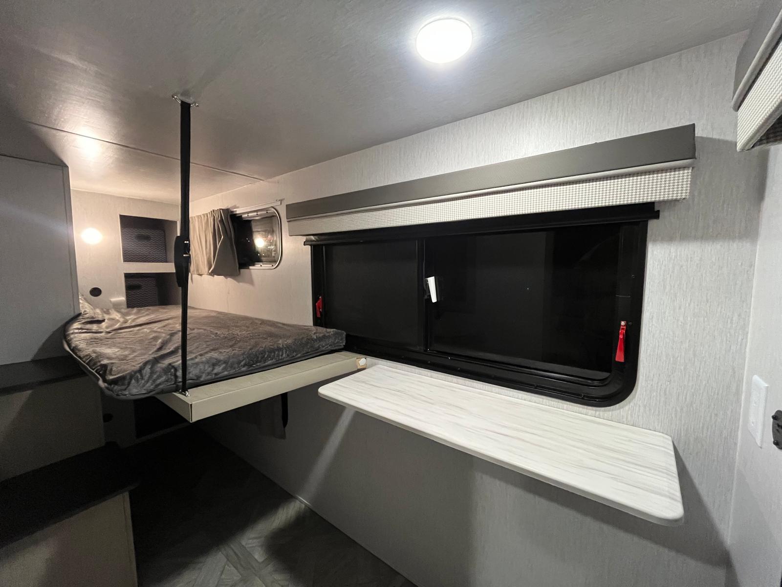 RV rental: Modern interior featuring an elevated bunk bed with strap support, large window with shades, and a compact shelf.. Forest River Wildwood 2024