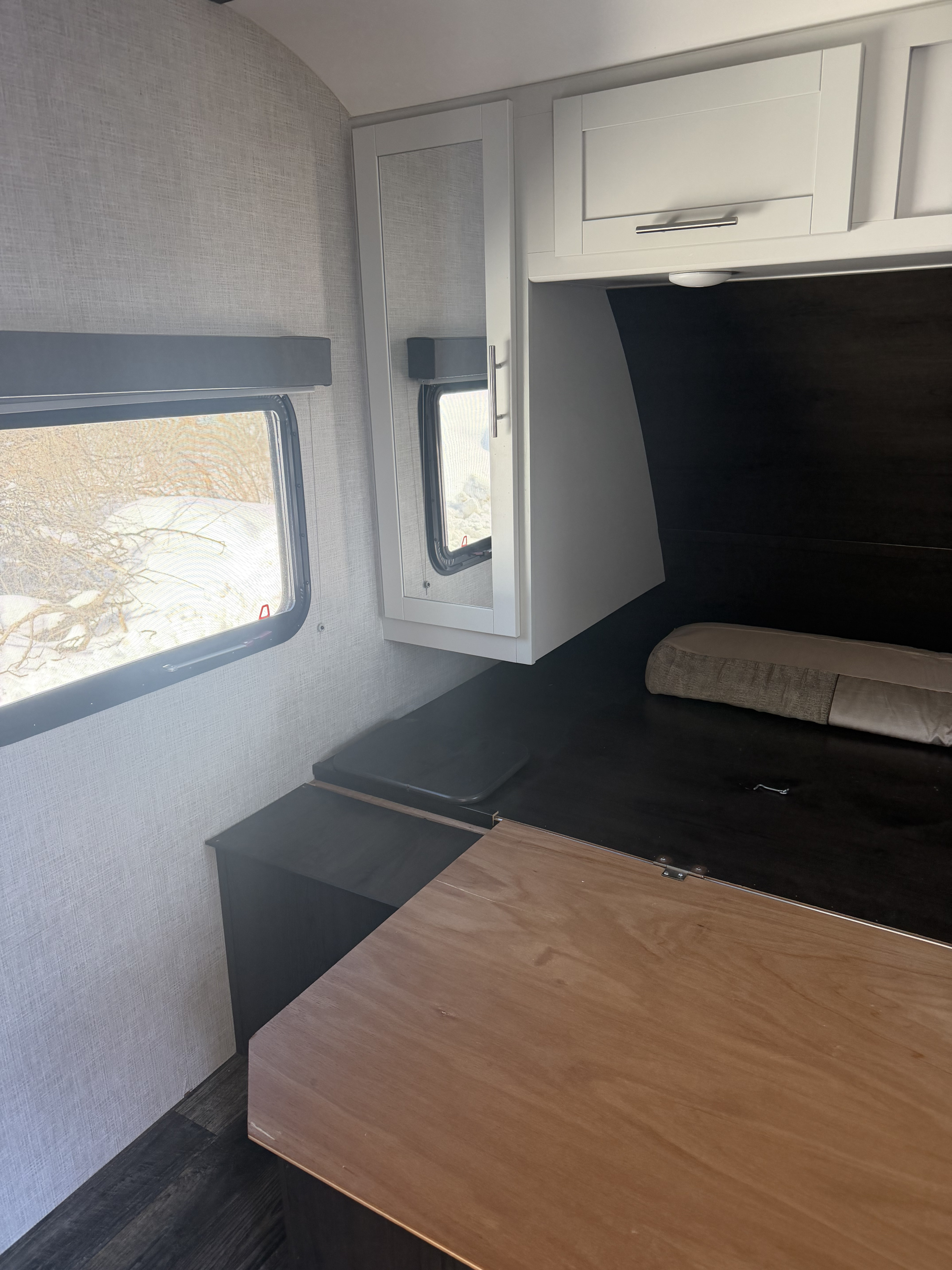 RV rental interior: convertible dinette/bed, white overhead cabinets, and a window with a snowy view outside.. Keystone RV Bullet Ultra Lite 2019